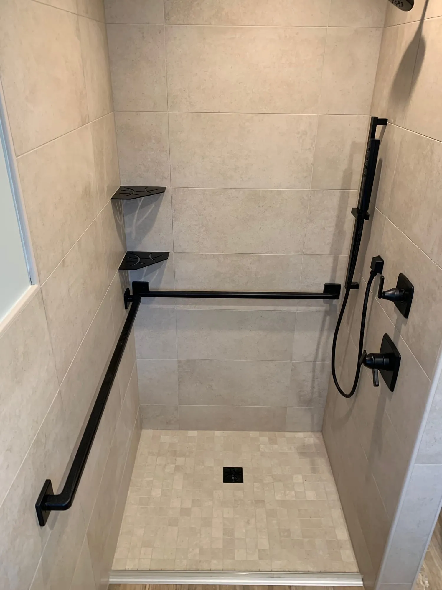 Accessible shower with matte black grab bars, a handheld shower on a slide bar and corner shelves