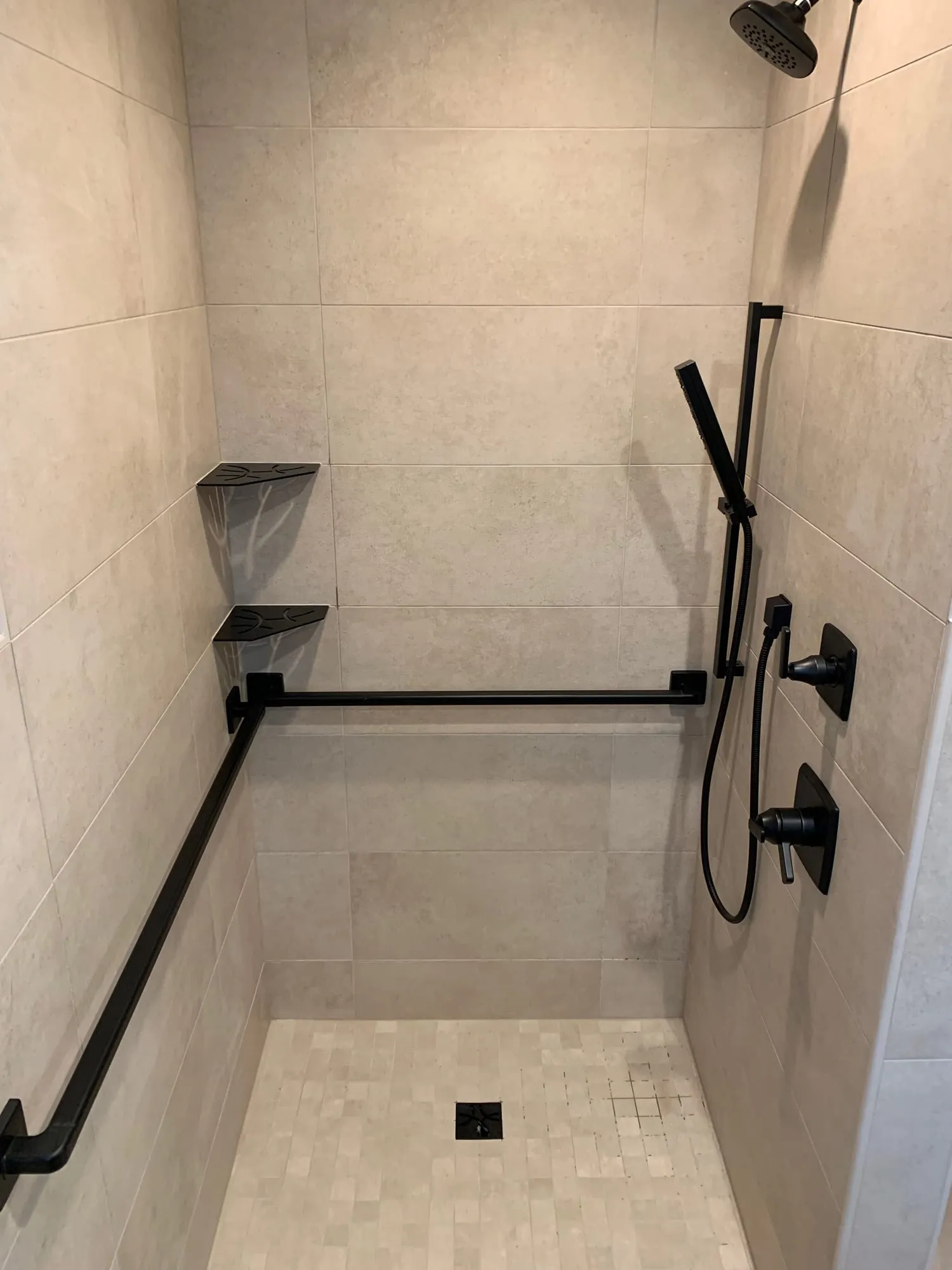 Shower with an L-shaped grab bar, matte black controls and mosaic floor tile