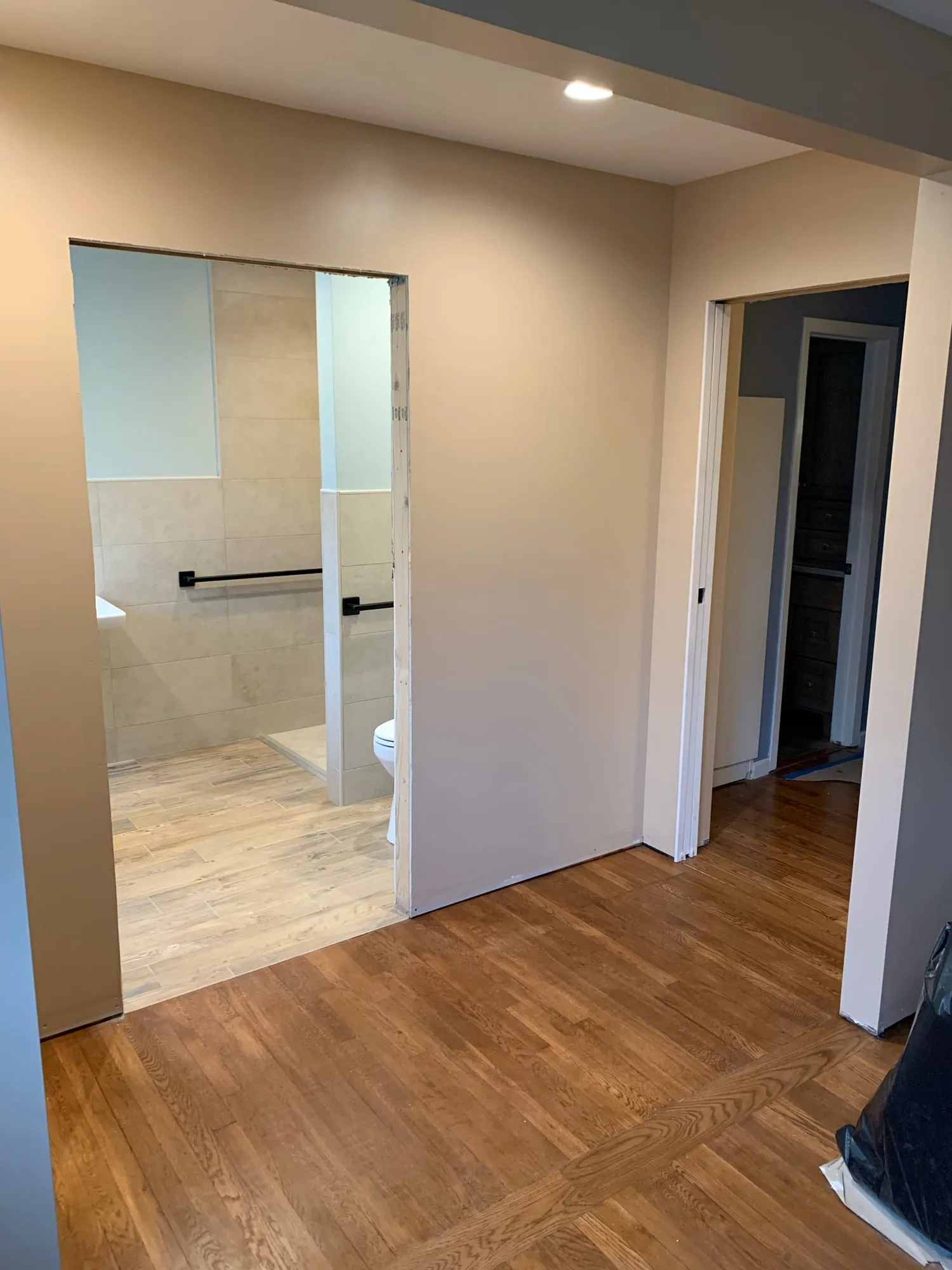 Wide doorway opening into a renovated accessible bathroom with grab bars and tile wainscot