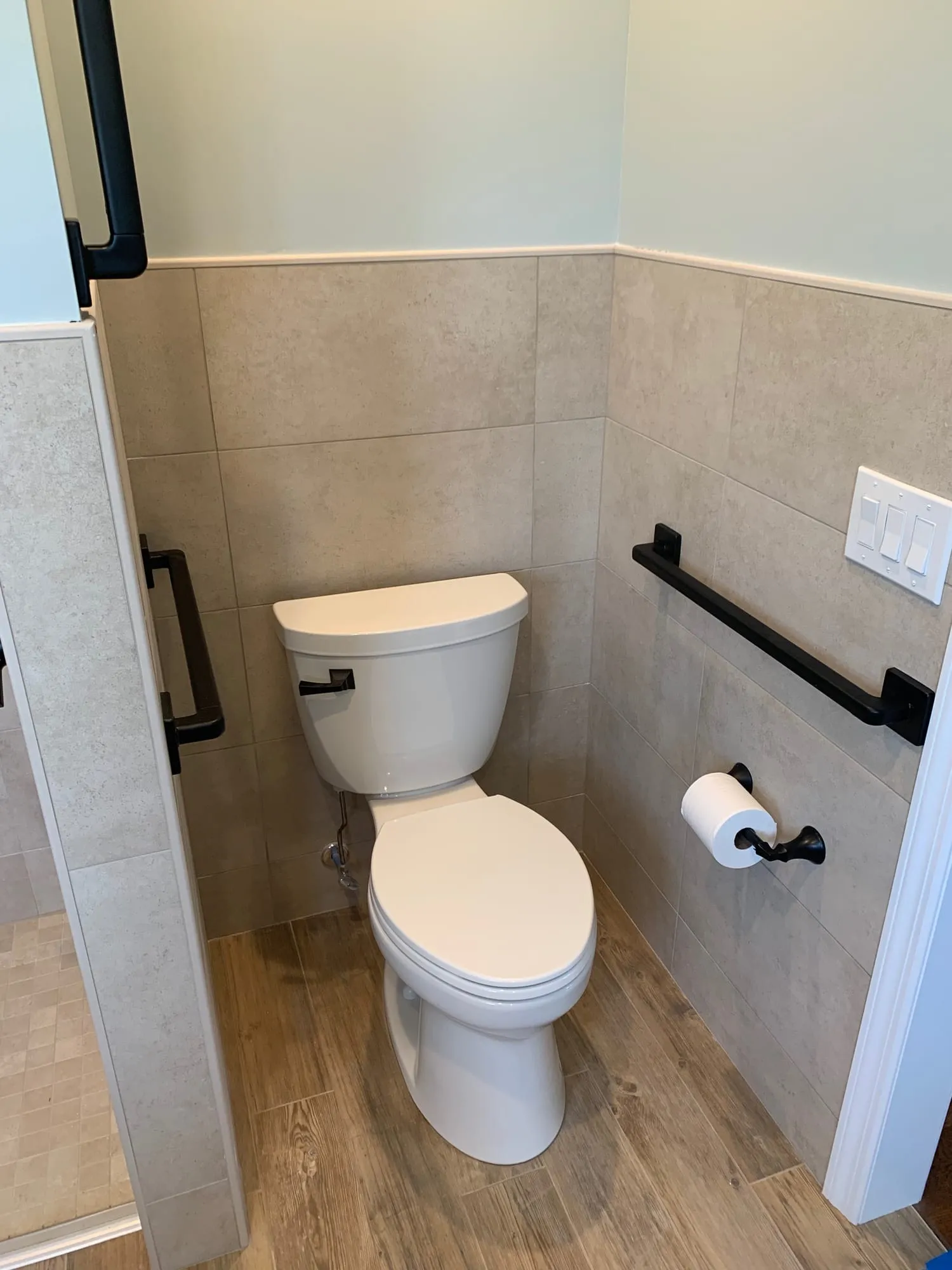 Toilet with grab bars on two walls and a tile wainscot