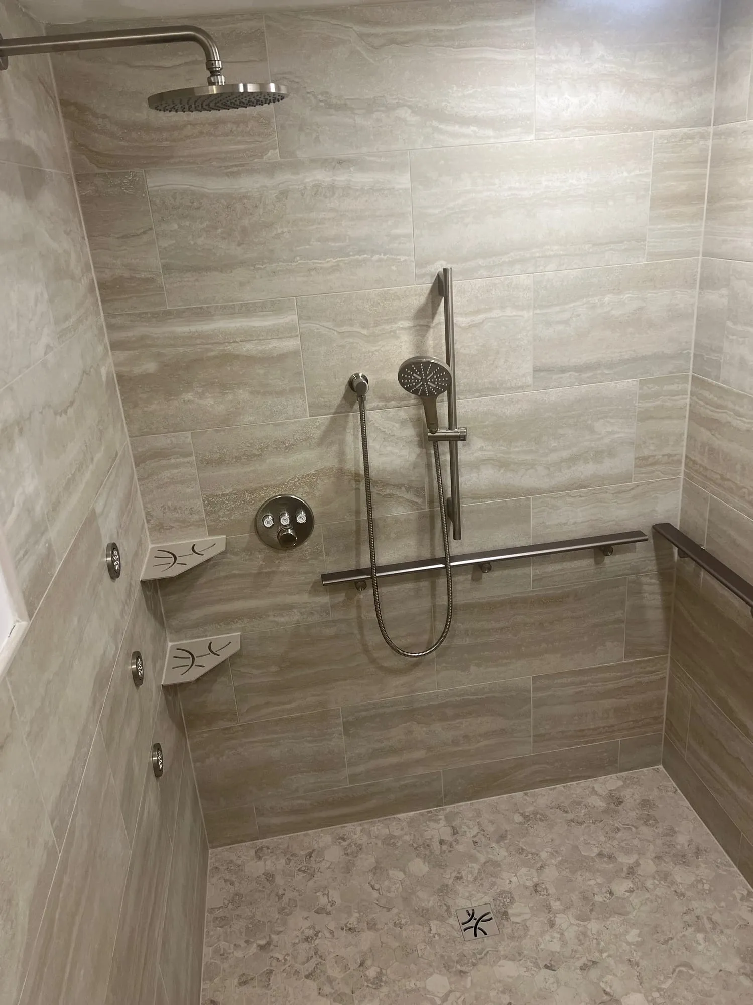 Accessible walk-in shower with a pebble floor, grab bars, handheld shower on a slide bar and corner shelves