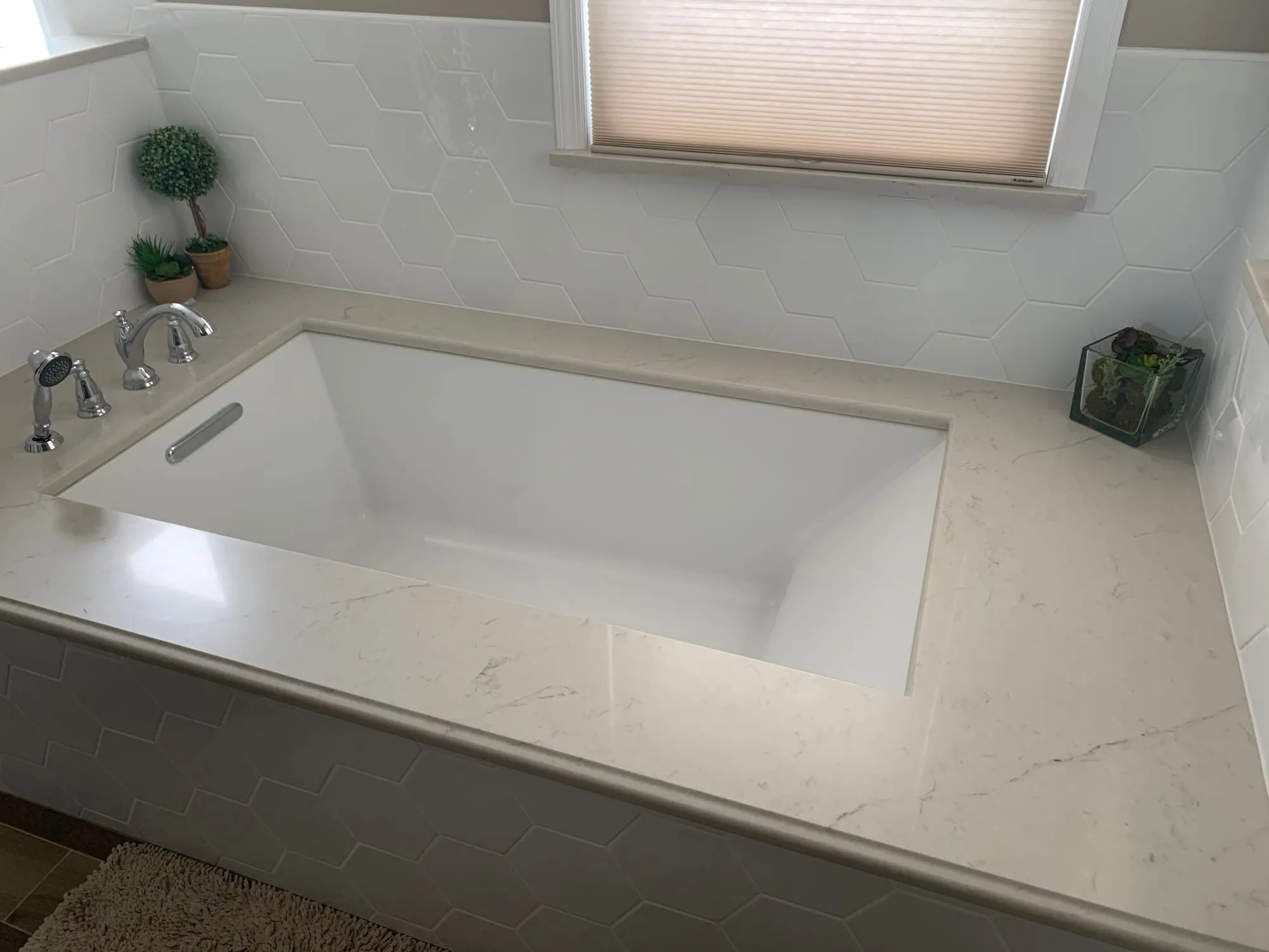 Undermount soaking tub set in a stone deck with white hexagon tile