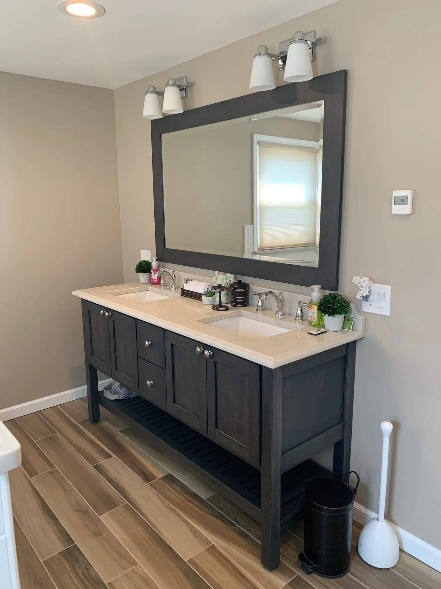 Babylon bathroom with a dark wood double vanity, stone top and wood-look tile flooring