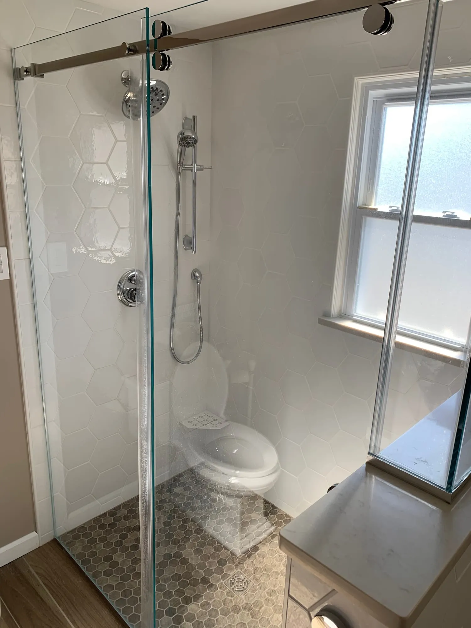 Frameless glass shower enclosure with hexagon tile and a handheld shower on a slide bar