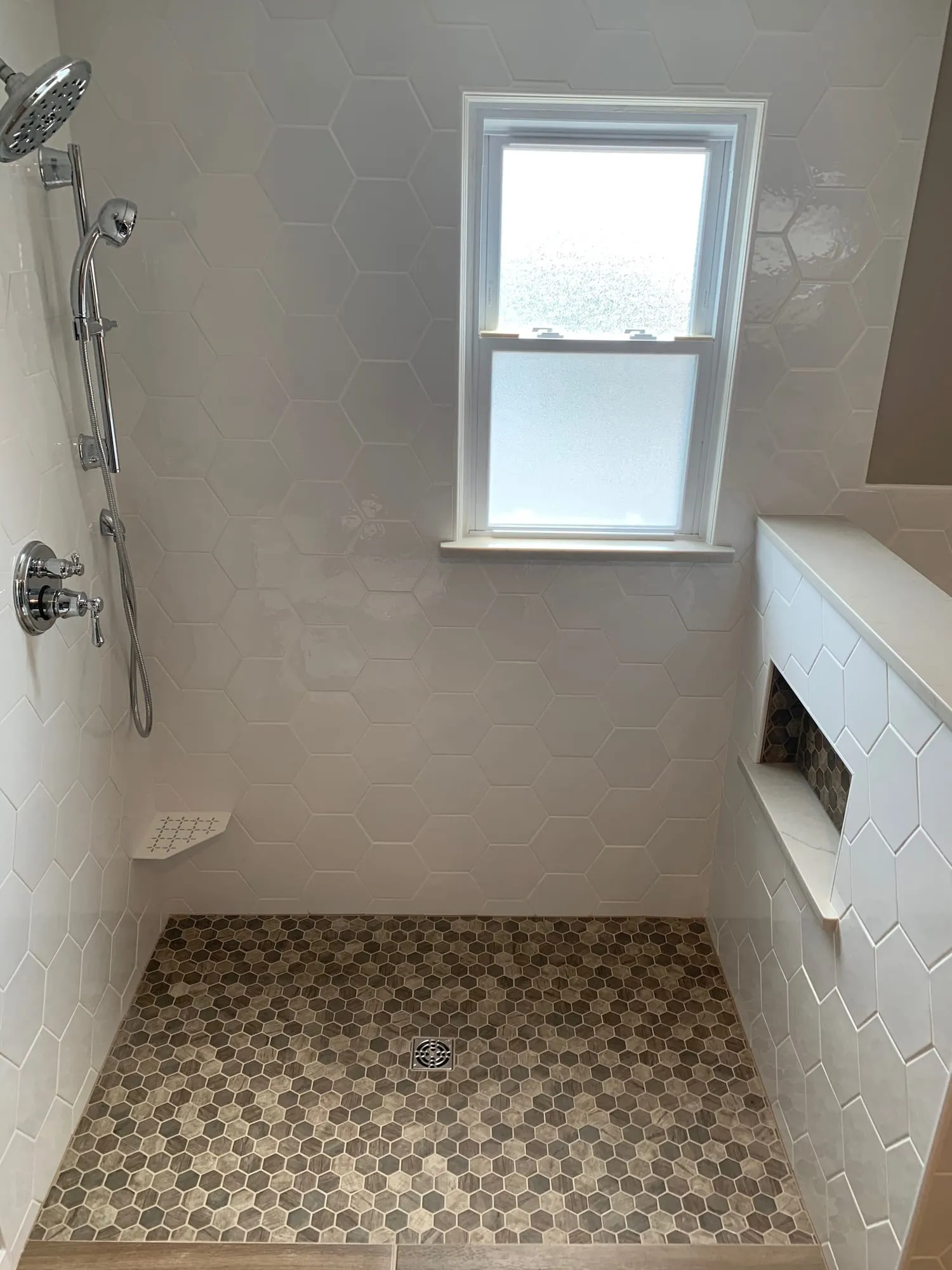 Shower with white wall tile, a hexagon mosaic floor, handheld shower and built-in niche