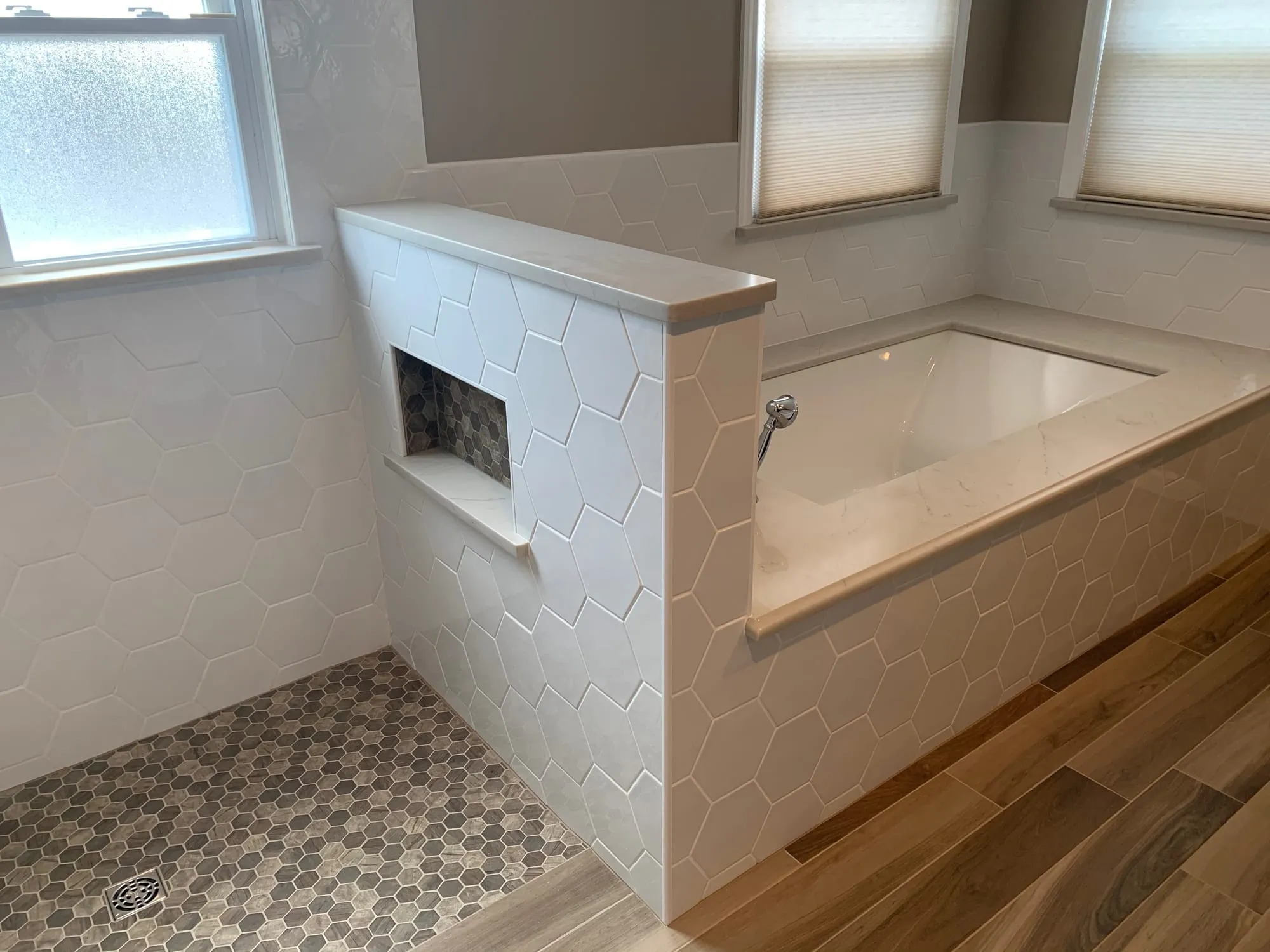 Walk-in shower behind a half wall with a recessed niche, next to the soaking tub