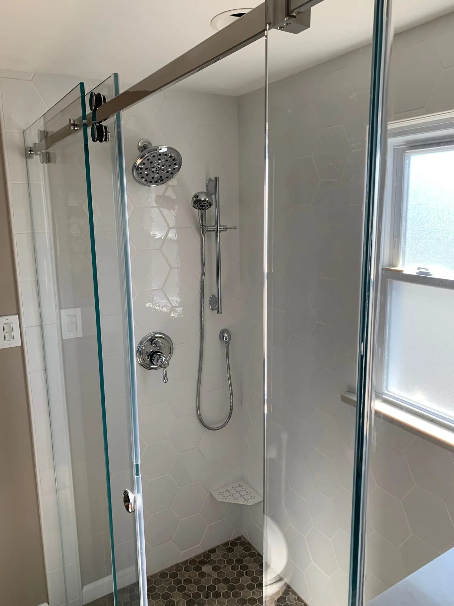 Shower with rain head, handheld shower and hexagon mosaic floor behind frameless glass