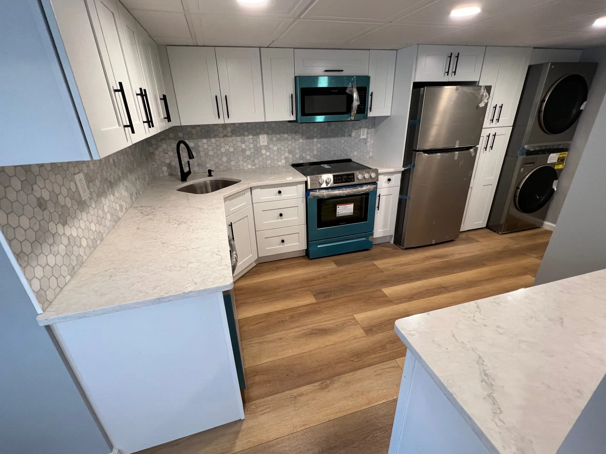 Basement kitchen run with a stacked washer and dryer beside the refrigerator