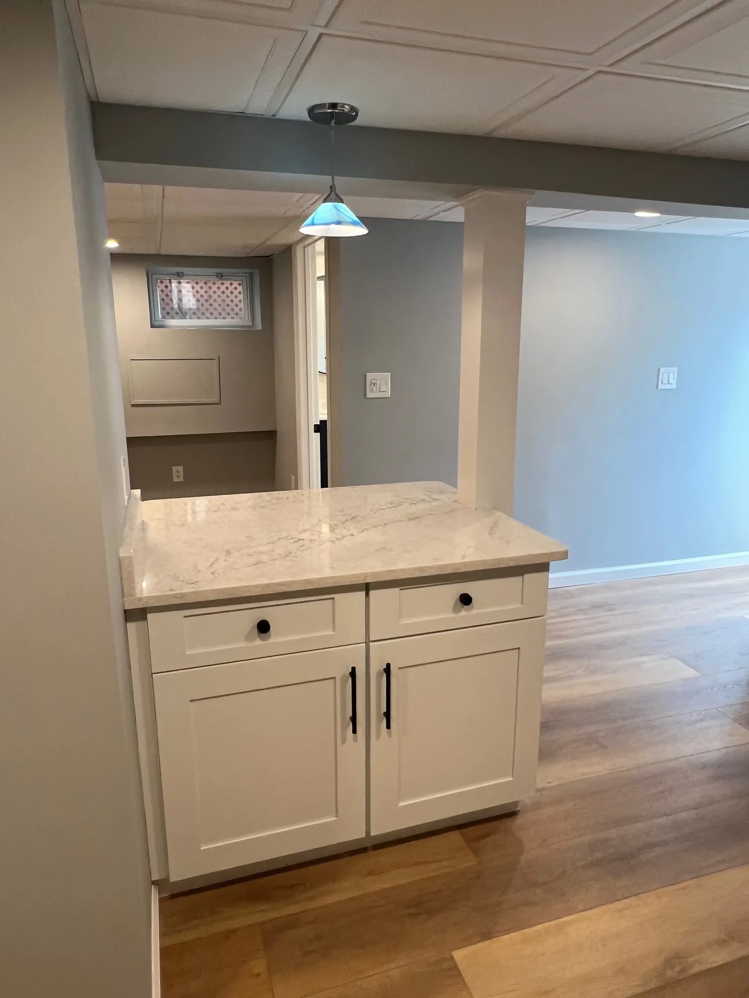 Kitchen island with white shaker cabinets and a marble-look top under a pendant light