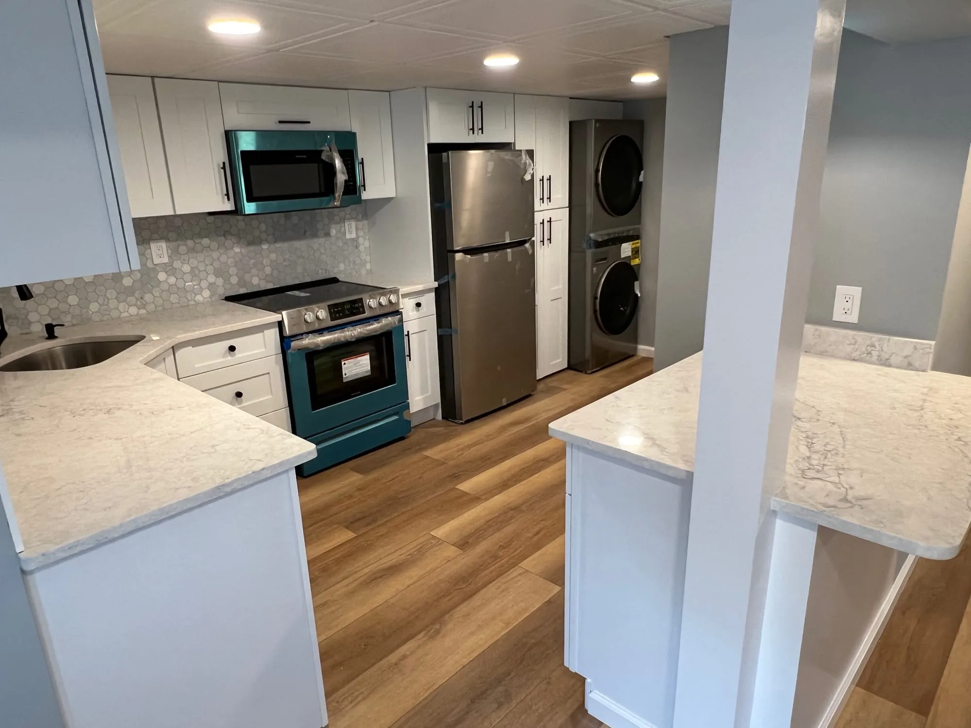 View into the basement kitchen past a marble-look counter, with wood-look plank flooring