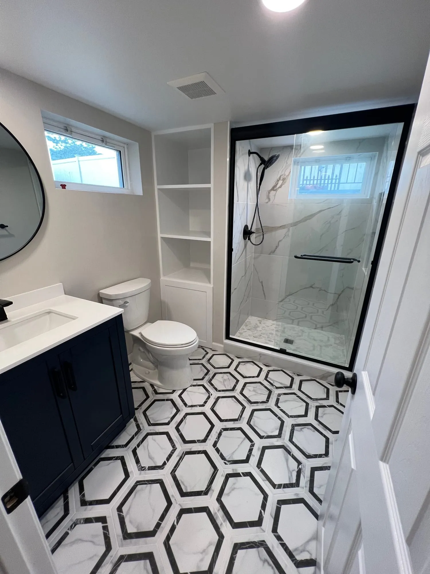 Basement bathroom with built-in open shelving beside a glass-enclosed shower