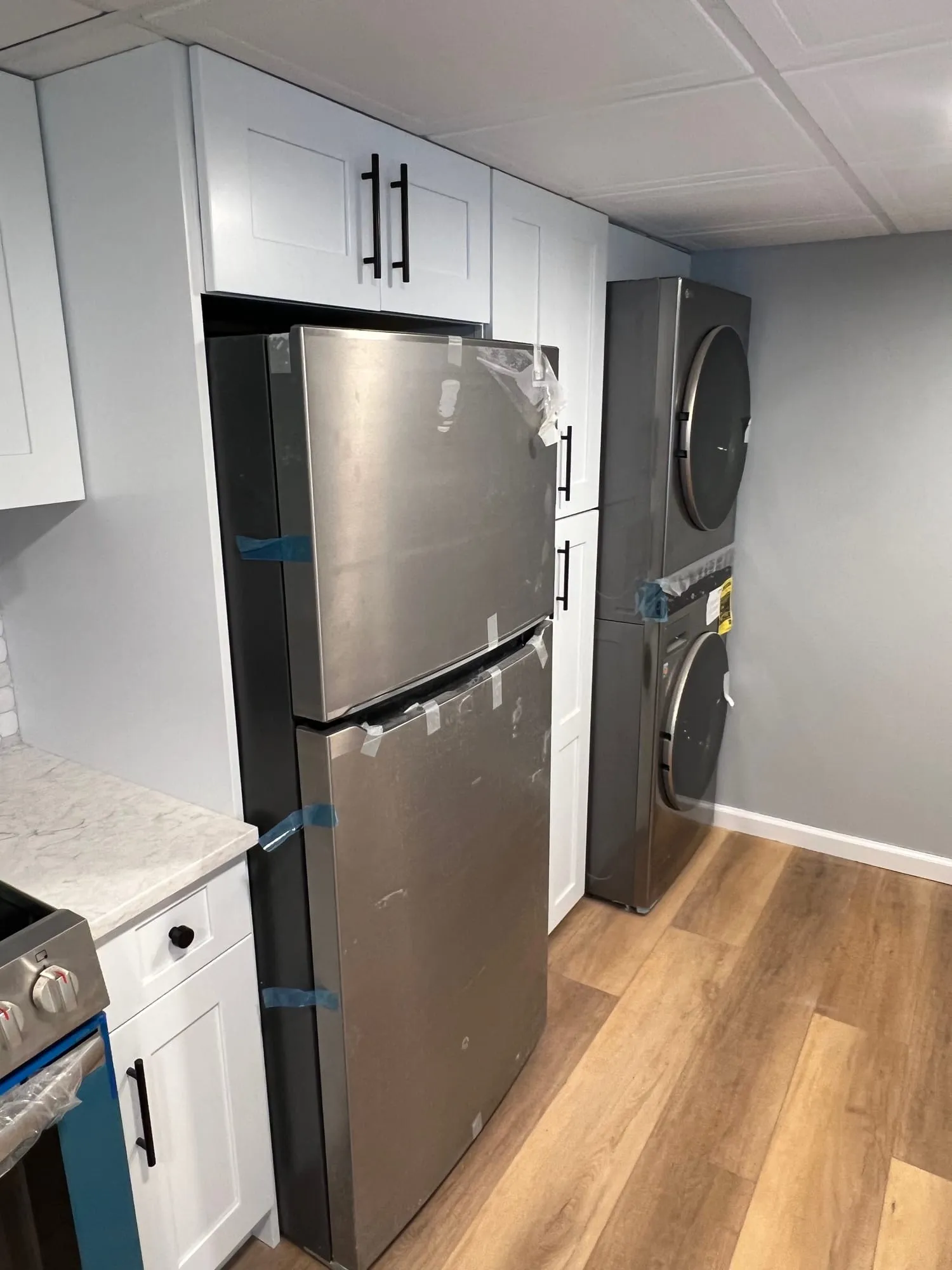 Tall white cabinetry around a refrigerator and stacked laundry in a Bay Shore basement