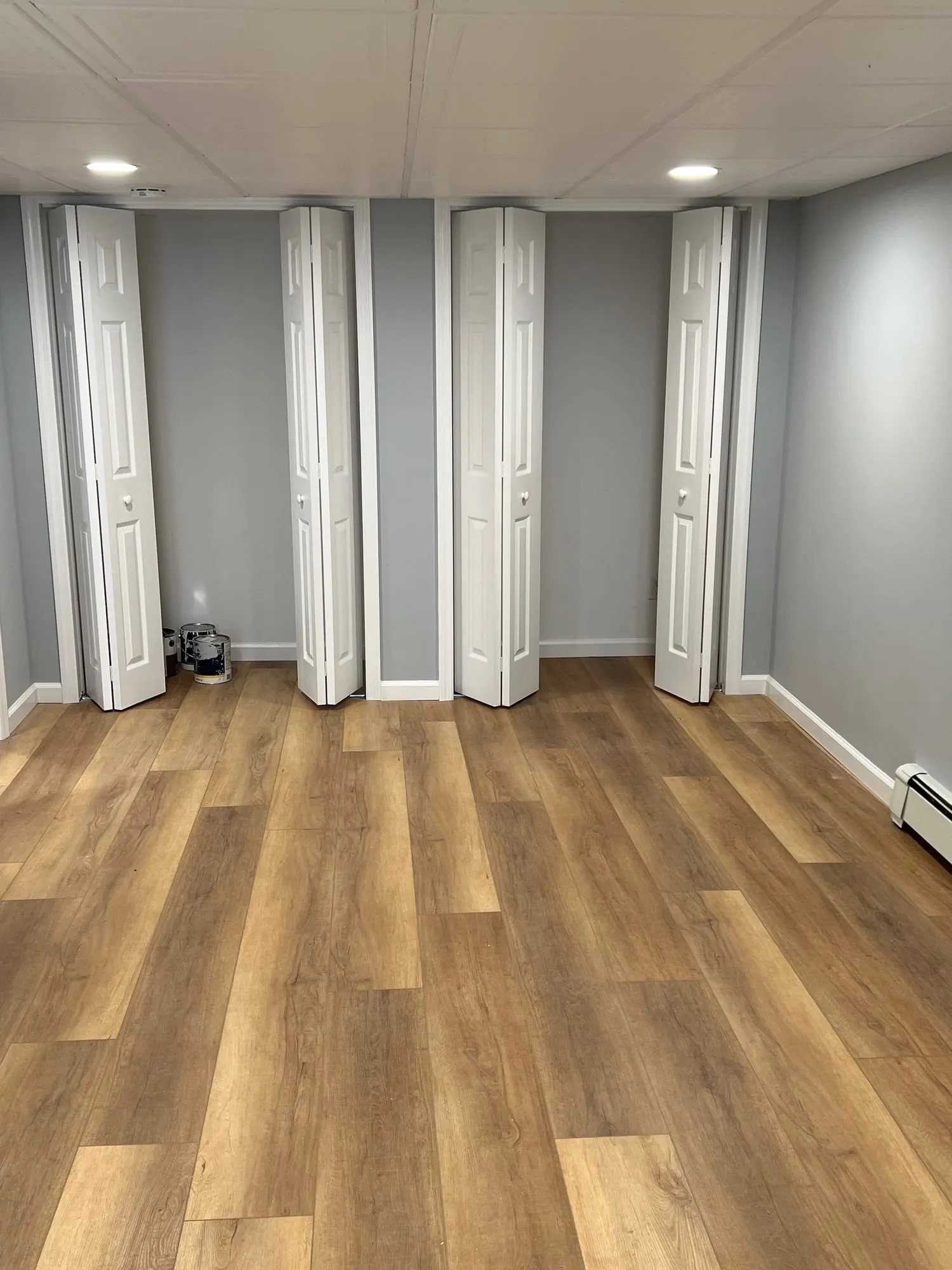 Finished basement room with wood-look flooring, recessed lights and closet doors