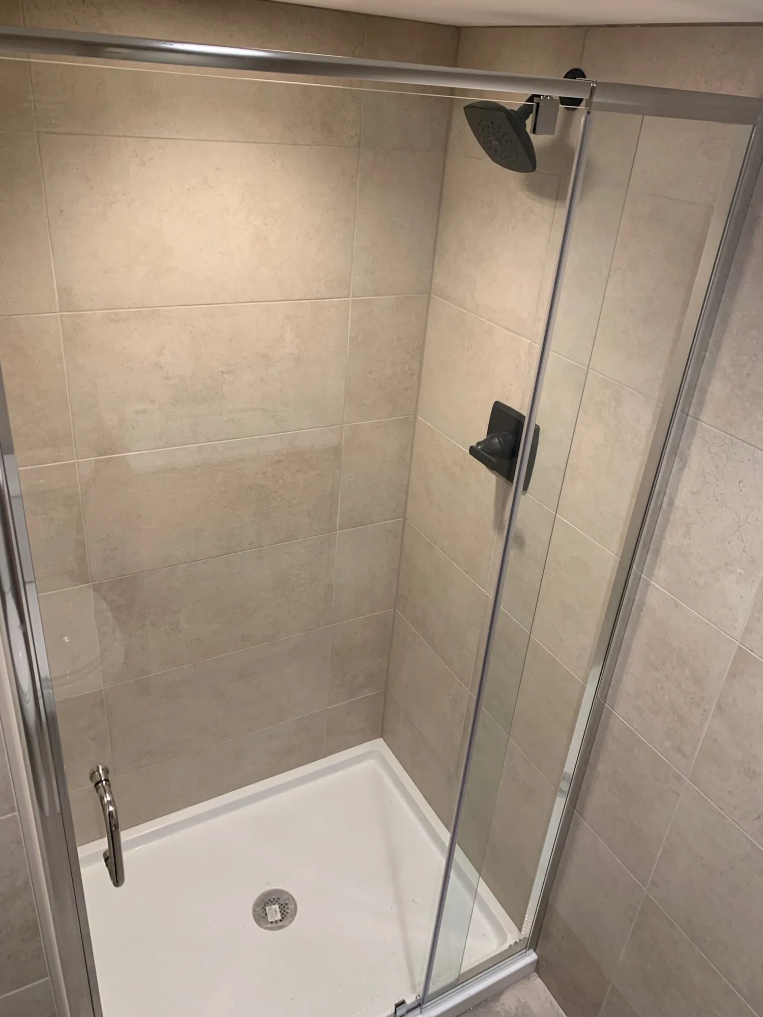 Basement shower with large-format stone-look tile, dark bronze fixtures and a sliding glass door