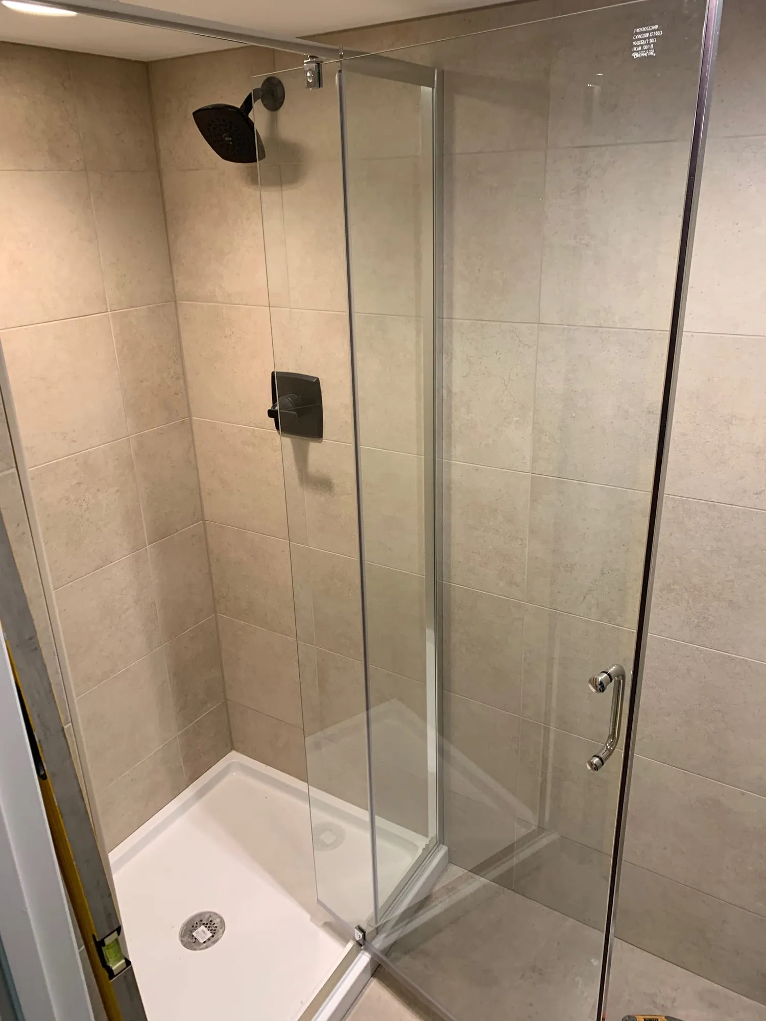 Shower stall with tiled walls, a white shower base and dark fixtures
