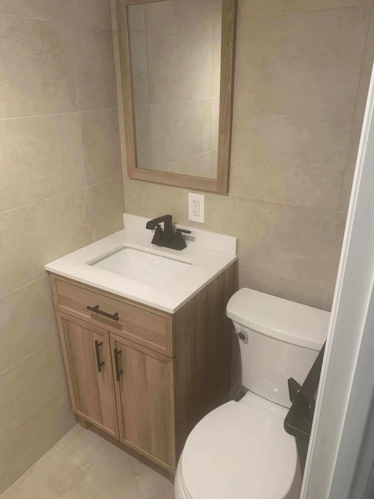 Compact vanity with a white top and dark faucet beside the toilet
