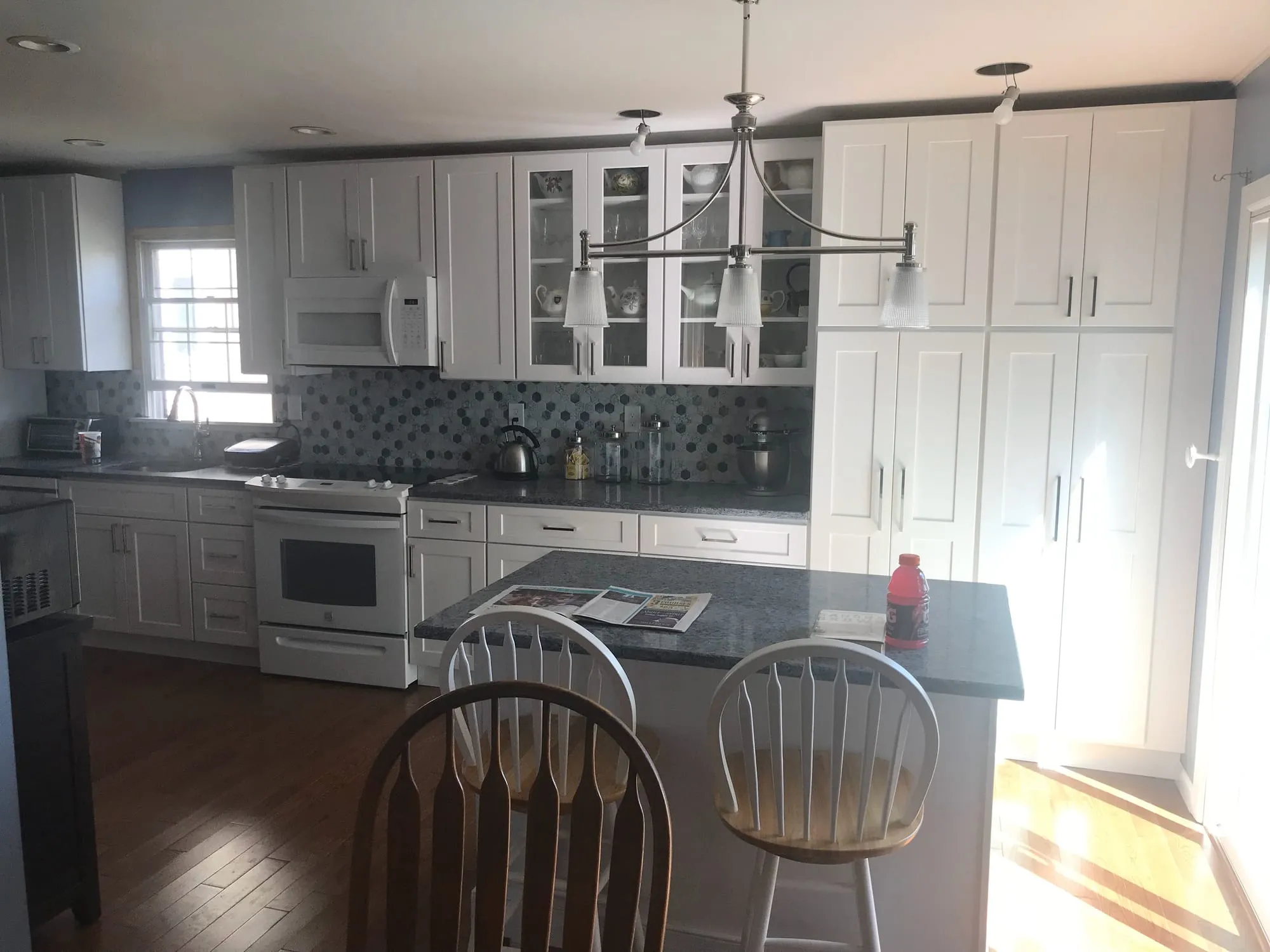 Open kitchen with white shaker cabinets, glass-front uppers, a mosaic tile backsplash and an island with seating