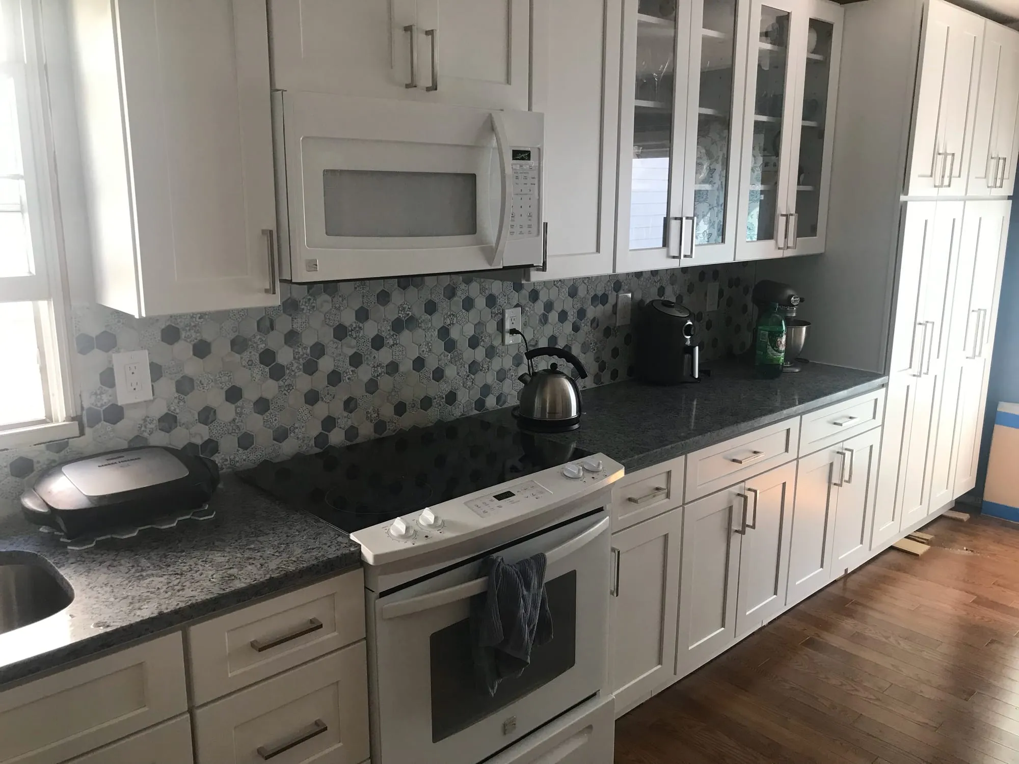 Glass-front upper cabinets and mosaic backsplash above dark stone countertops
