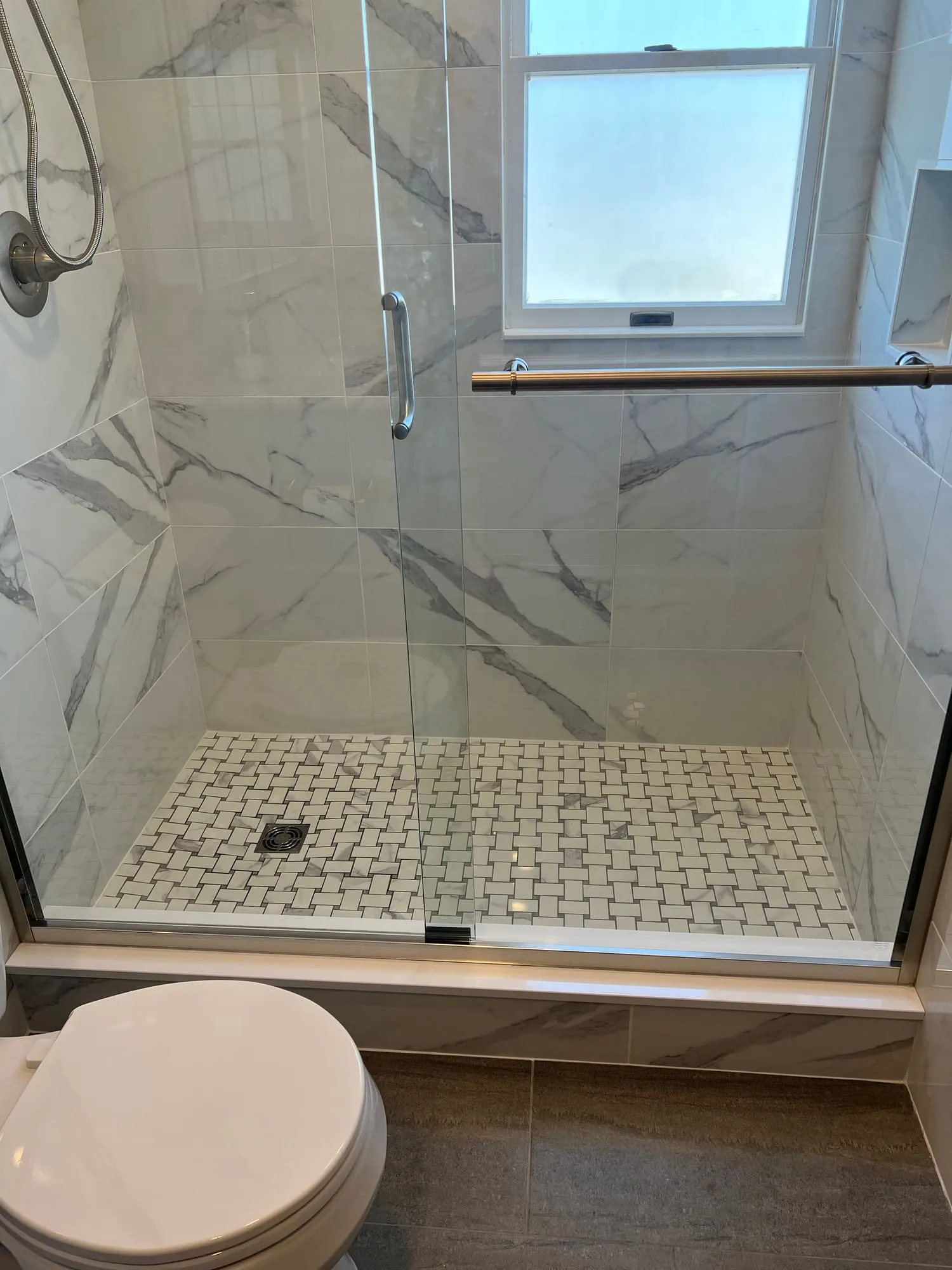 Walk-in shower with marble-look tile, a basketweave mosaic floor and sliding glass door