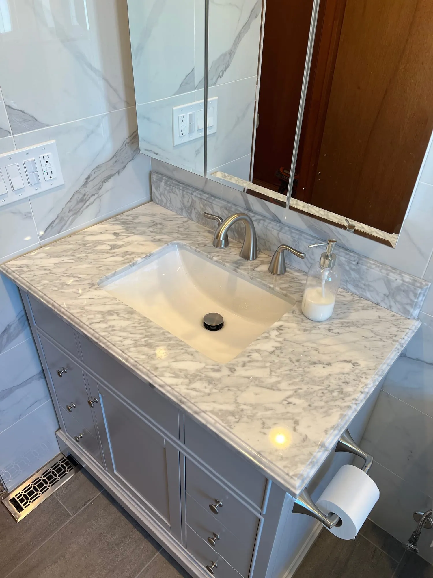 Gray vanity with a marble top and undermount sink against marble-look tile