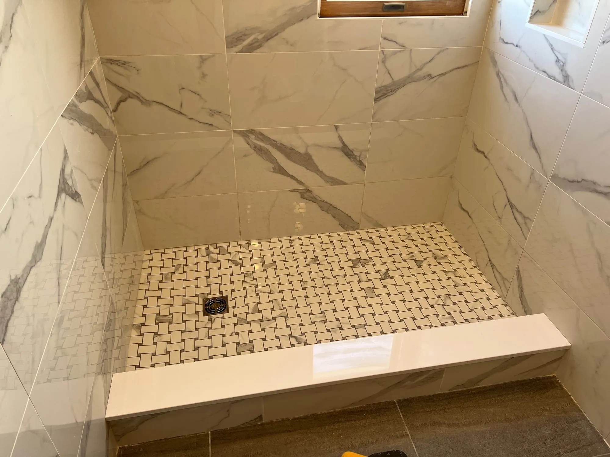 Tiled shower with marble-look walls, mosaic floor and a stone curb before the glass door