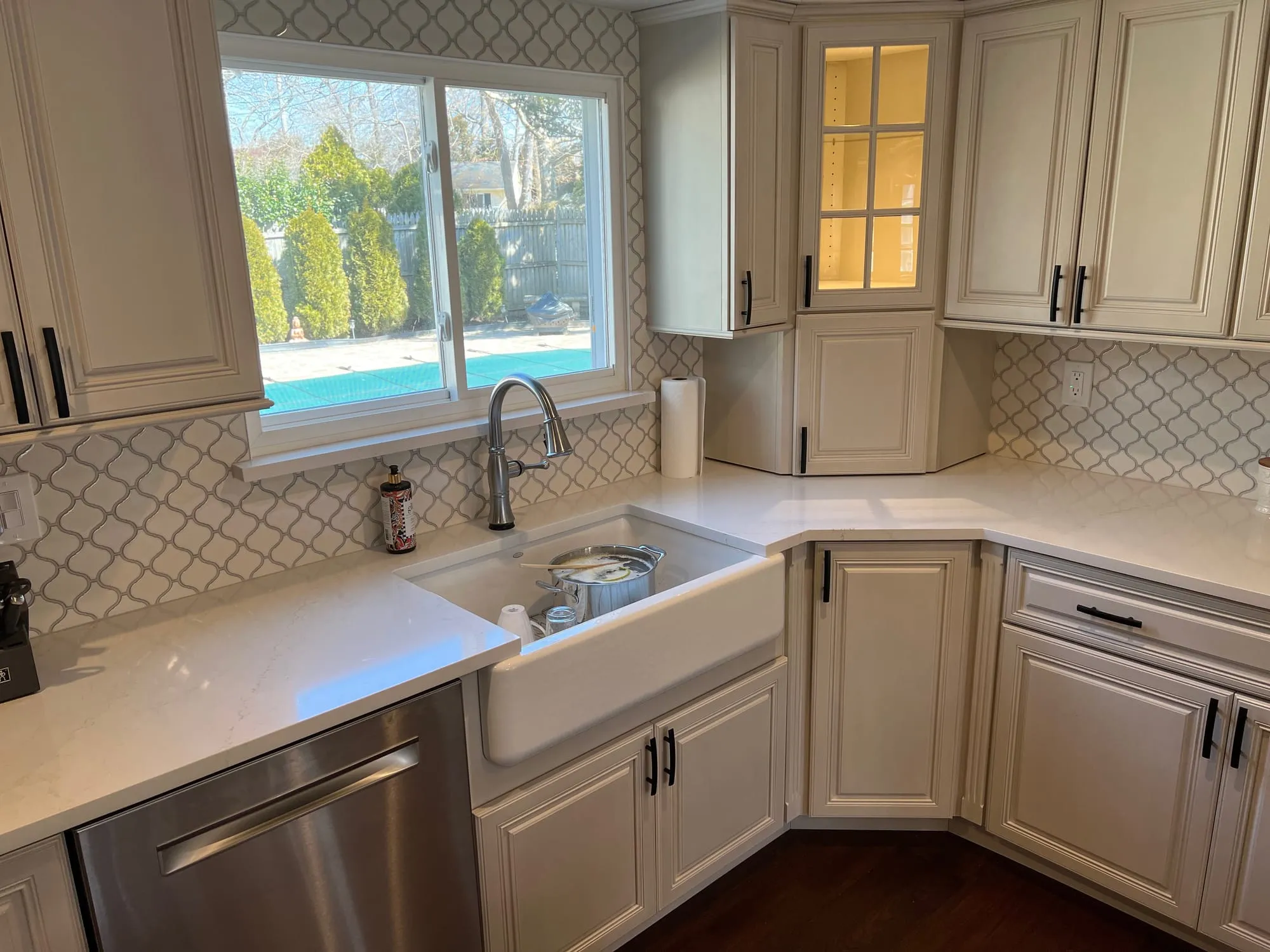 Renovated kitchen with painted raised-panel cabinets, arabesque tile backsplash, white countertops and a farmhouse sink beneath a window