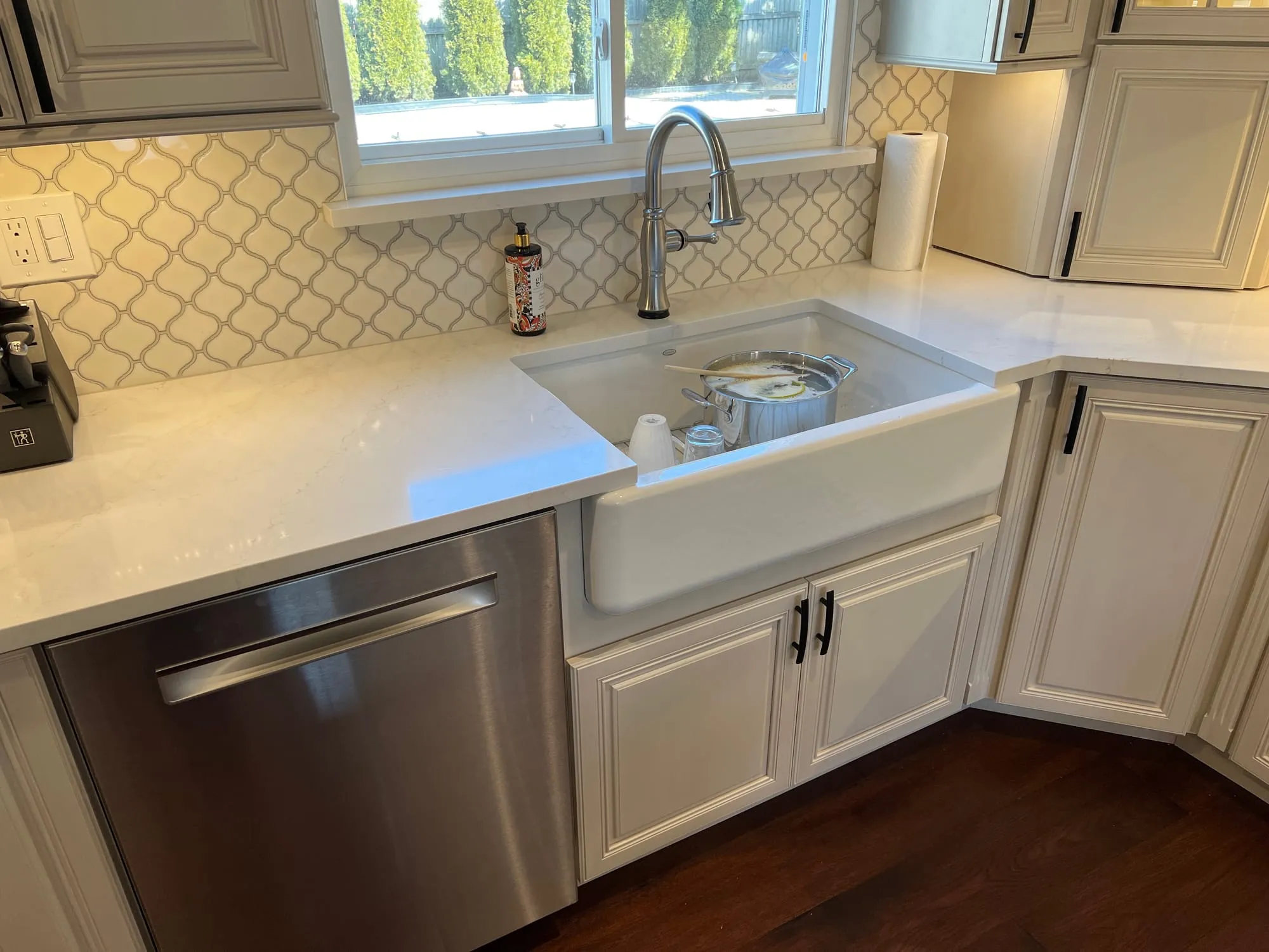 Farmhouse sink and stainless dishwasher set into white countertops with arabesque tile