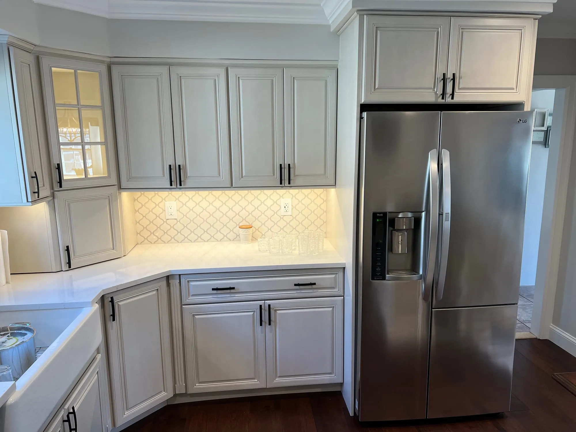 Stainless refrigerator framed by painted cabinetry and a glass-front corner cabinet
