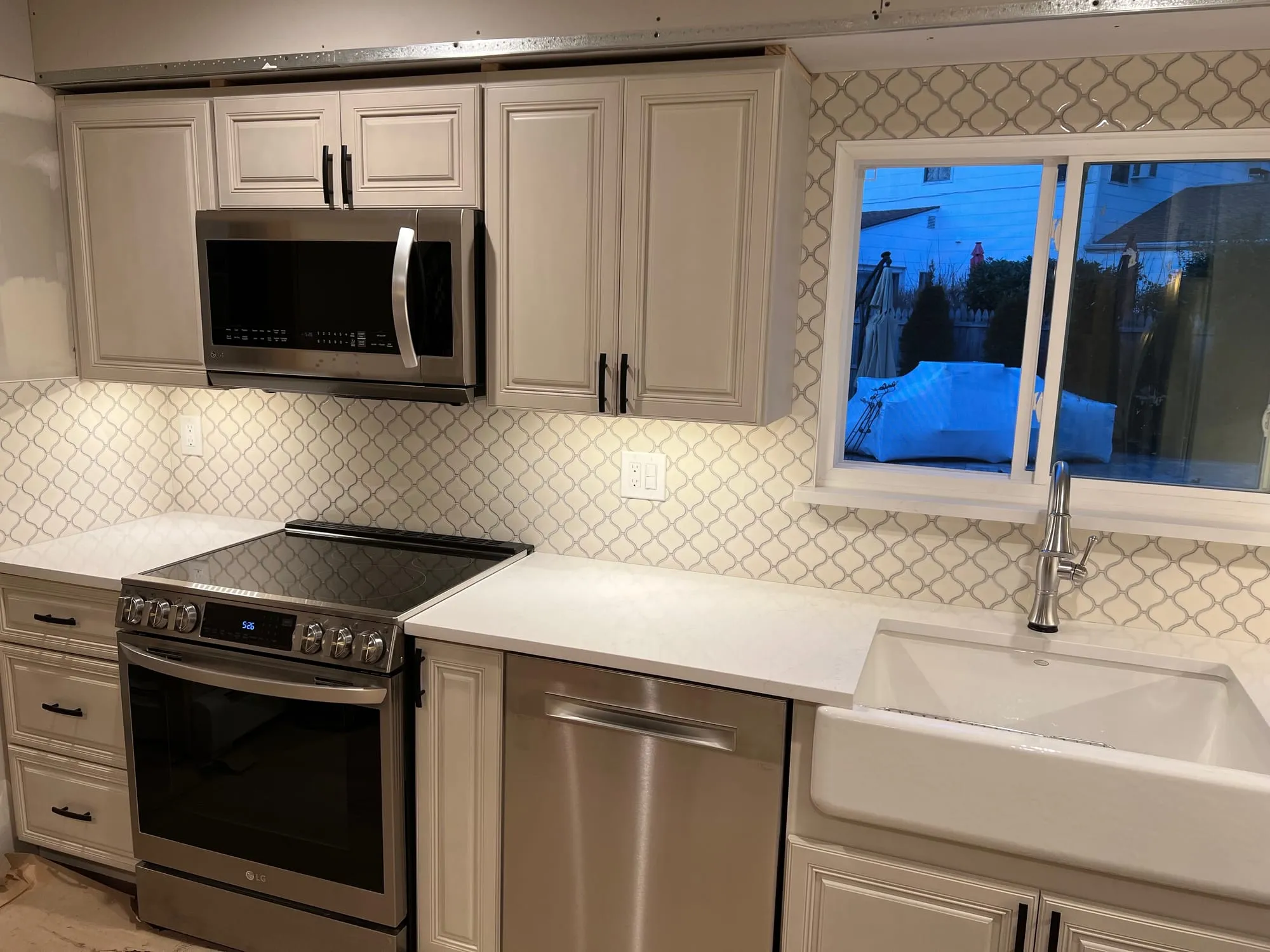 The same kitchen after renovation, with painted cabinets, white countertops and a farmhouse sink