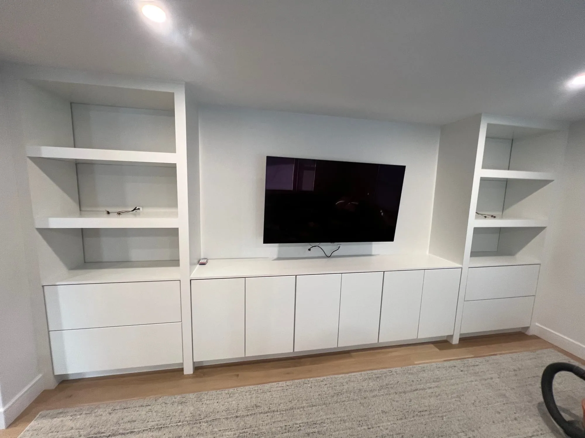 Finished East Hills basement with a full-width built-in media wall and lit open shelving