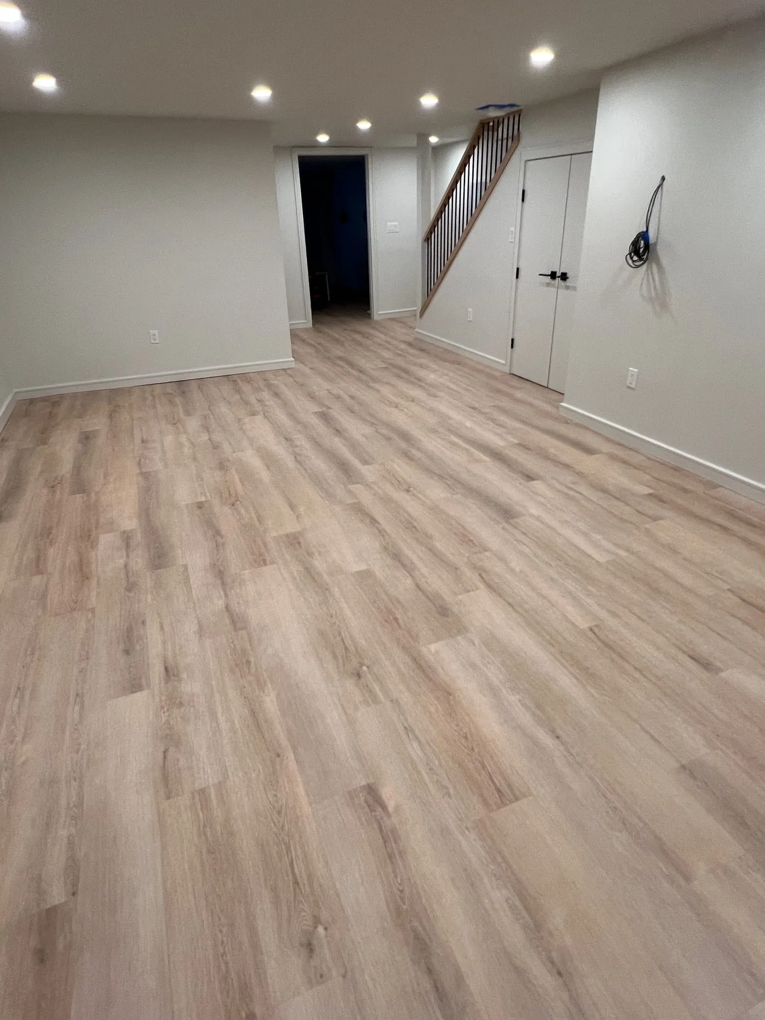 Open finished basement with wood-look plank flooring, recessed lighting and a new staircase