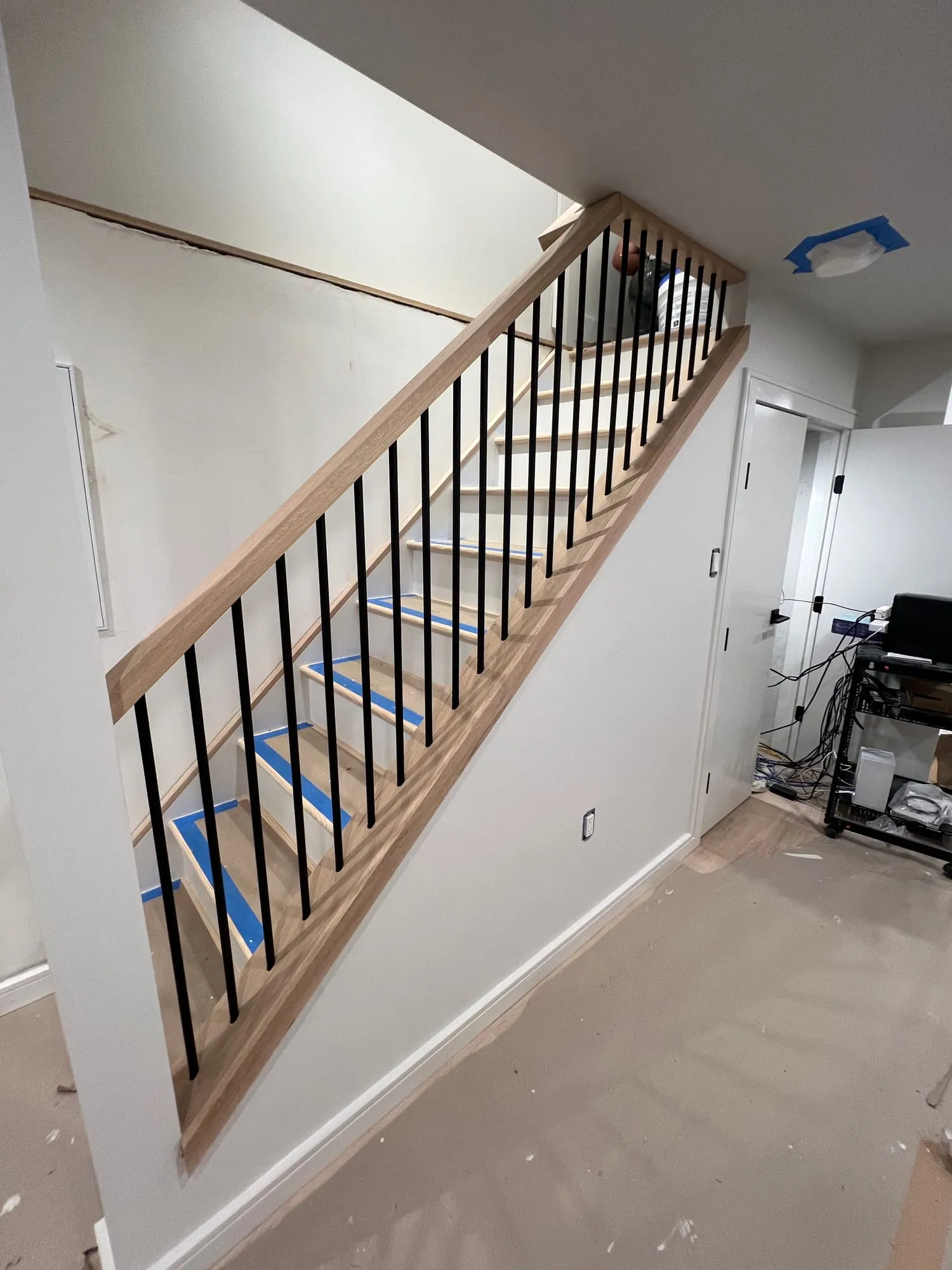 New staircase with wood handrail and black metal balusters, treads taped for protection