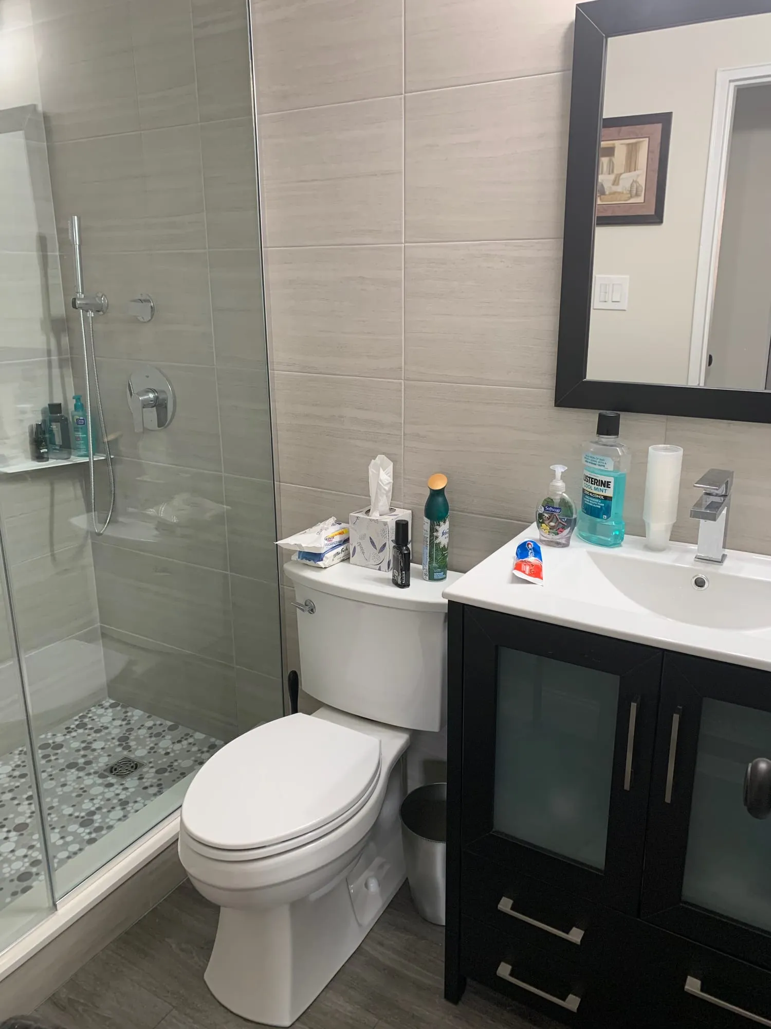 Renovated bathroom with large-format gray tile, a glass shower enclosure and a dark vanity
