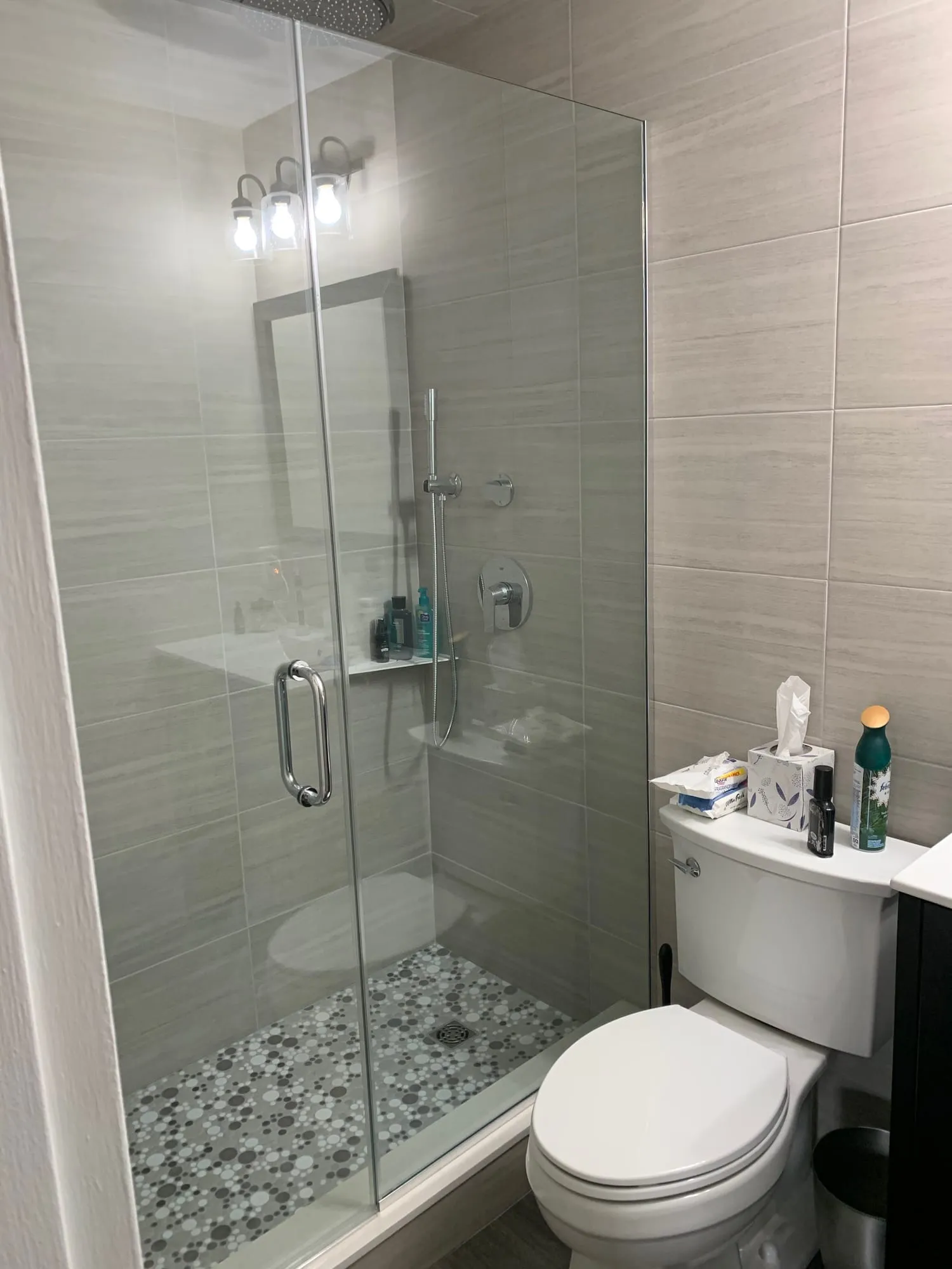 Glass-enclosed shower with linear gray wall tile and a pebble mosaic floor
