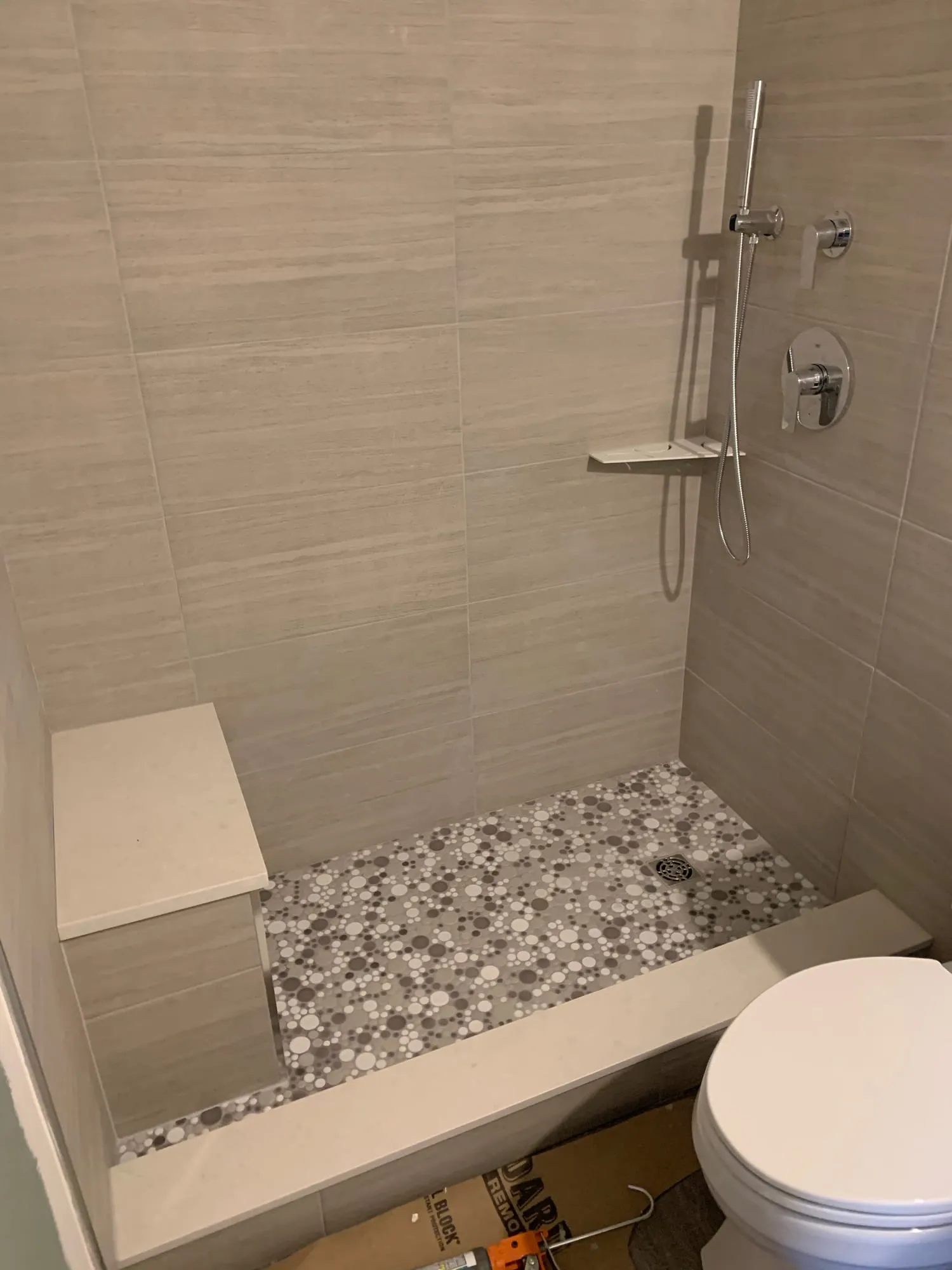 Shower in progress, with large-format wall tile, a pebble floor and a built-in bench before the glass was installed