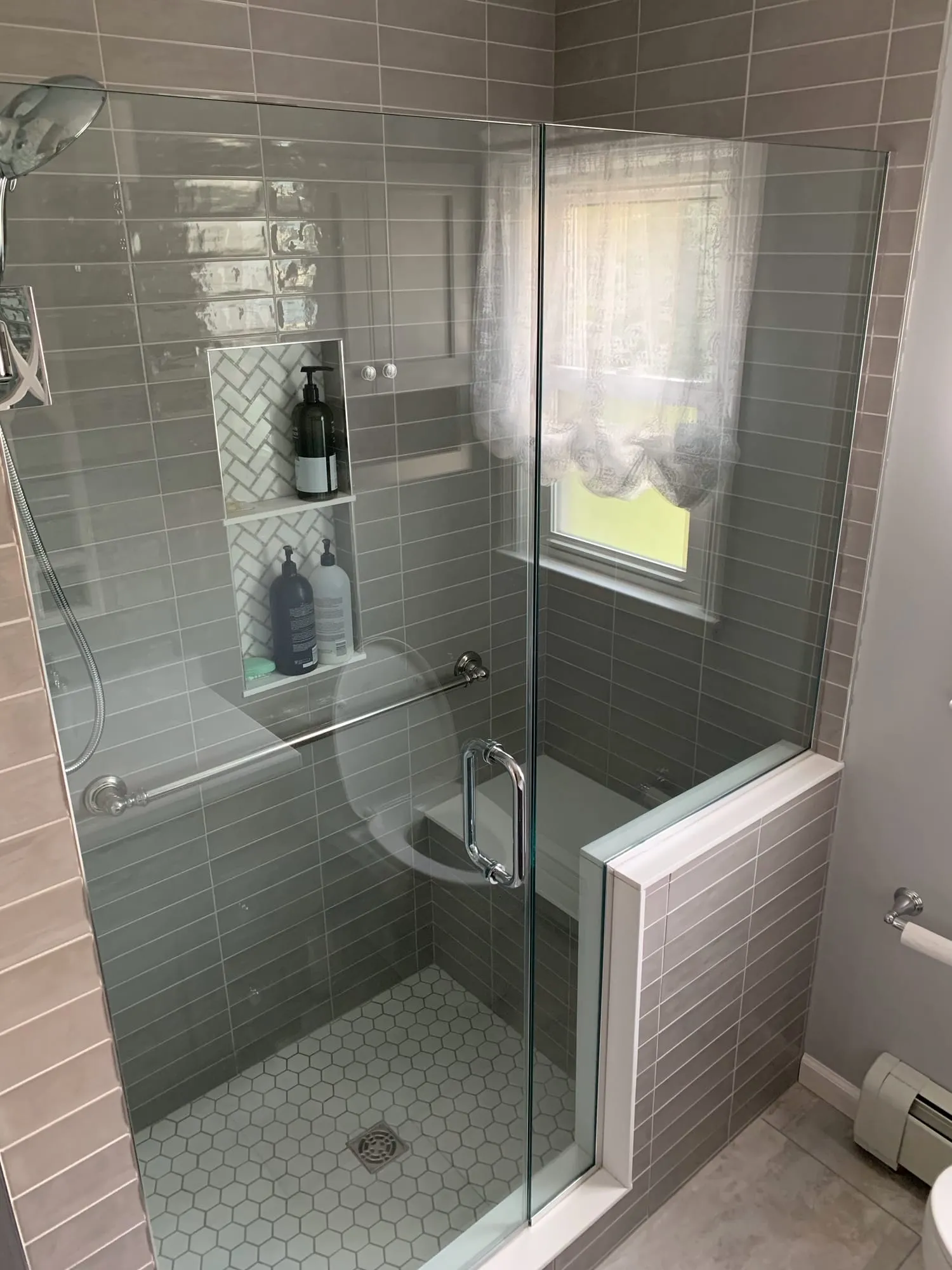 Walk-in shower with gray glass subway tile, a recessed niche, built-in bench and frameless glass