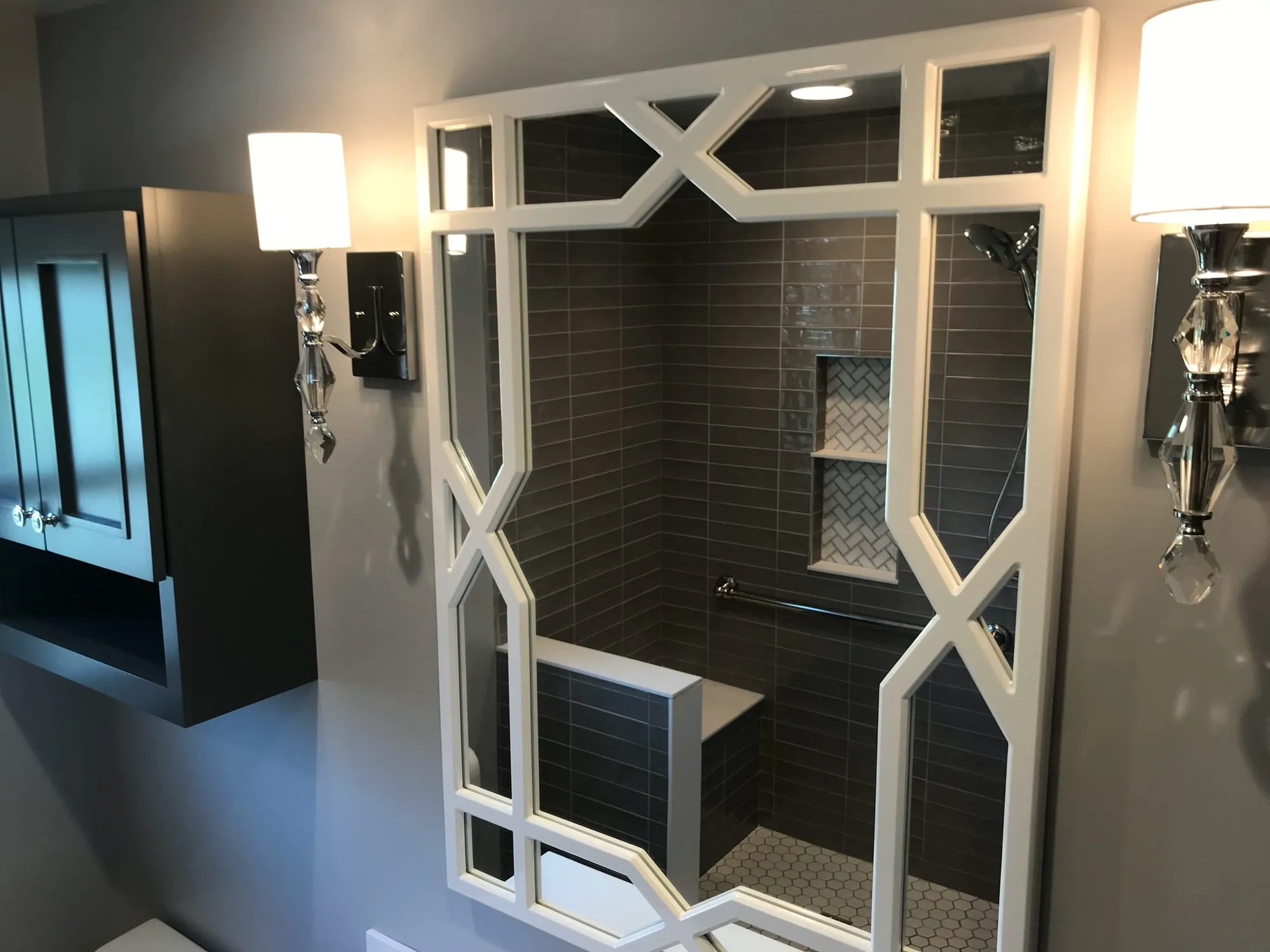 Lattice-framed mirror and wall sconces reflecting the tiled shower