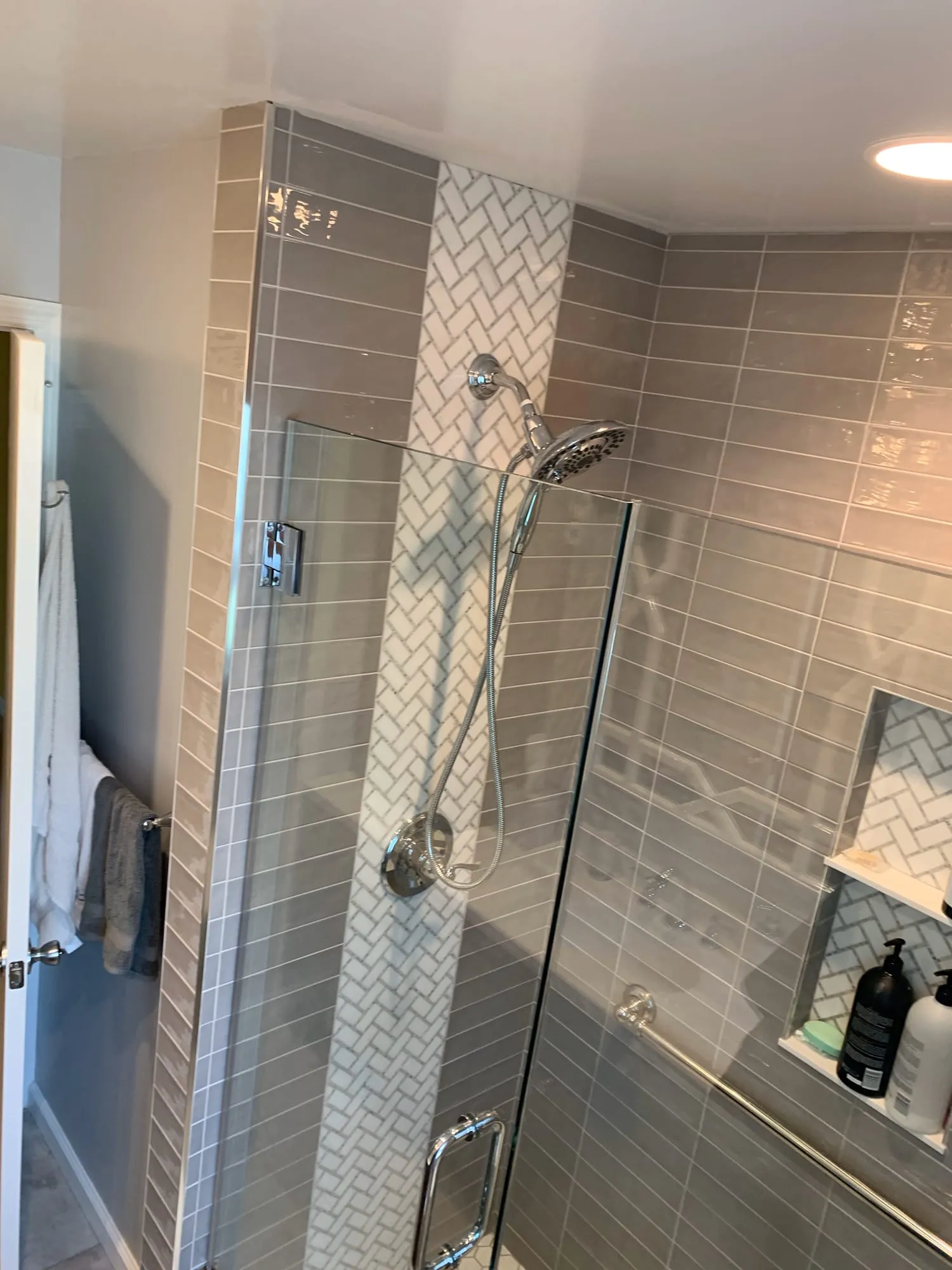 Shower with a vertical white herringbone accent stripe, handheld shower and grab bar