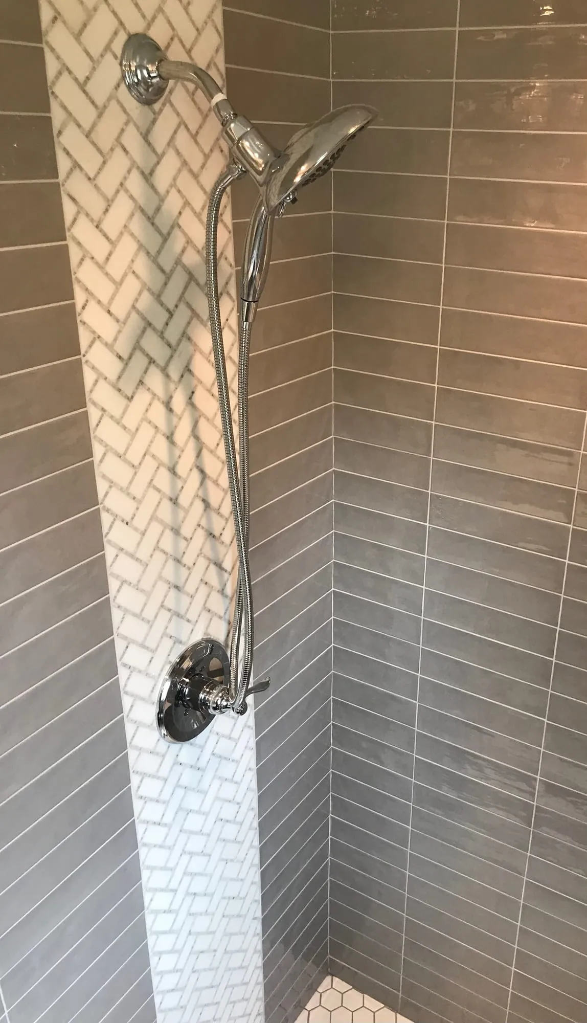 Gray subway tile with a white herringbone accent column at the shower valve