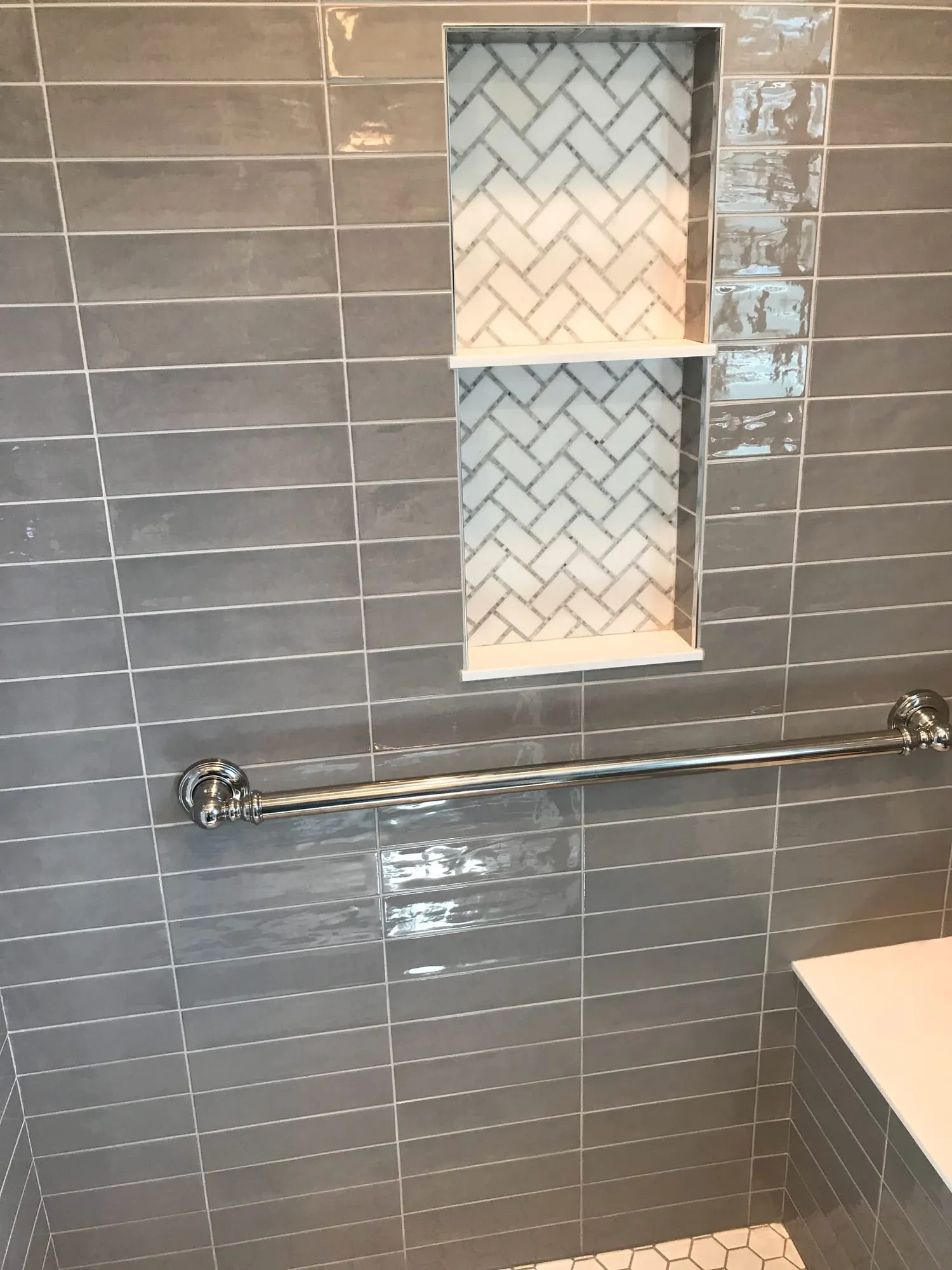 Gray glass subway tile shower with a herringbone niche reflected in a lattice mirror