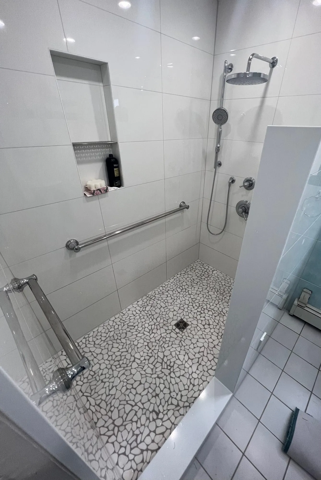 Walk-in shower with white large-format tile, a pebble mosaic floor, grab bar and recessed niche