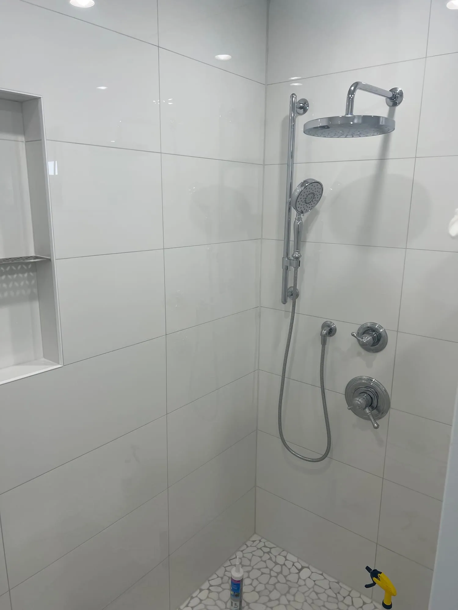 Rain head, handheld shower on a slide bar and a recessed niche in a white tiled shower