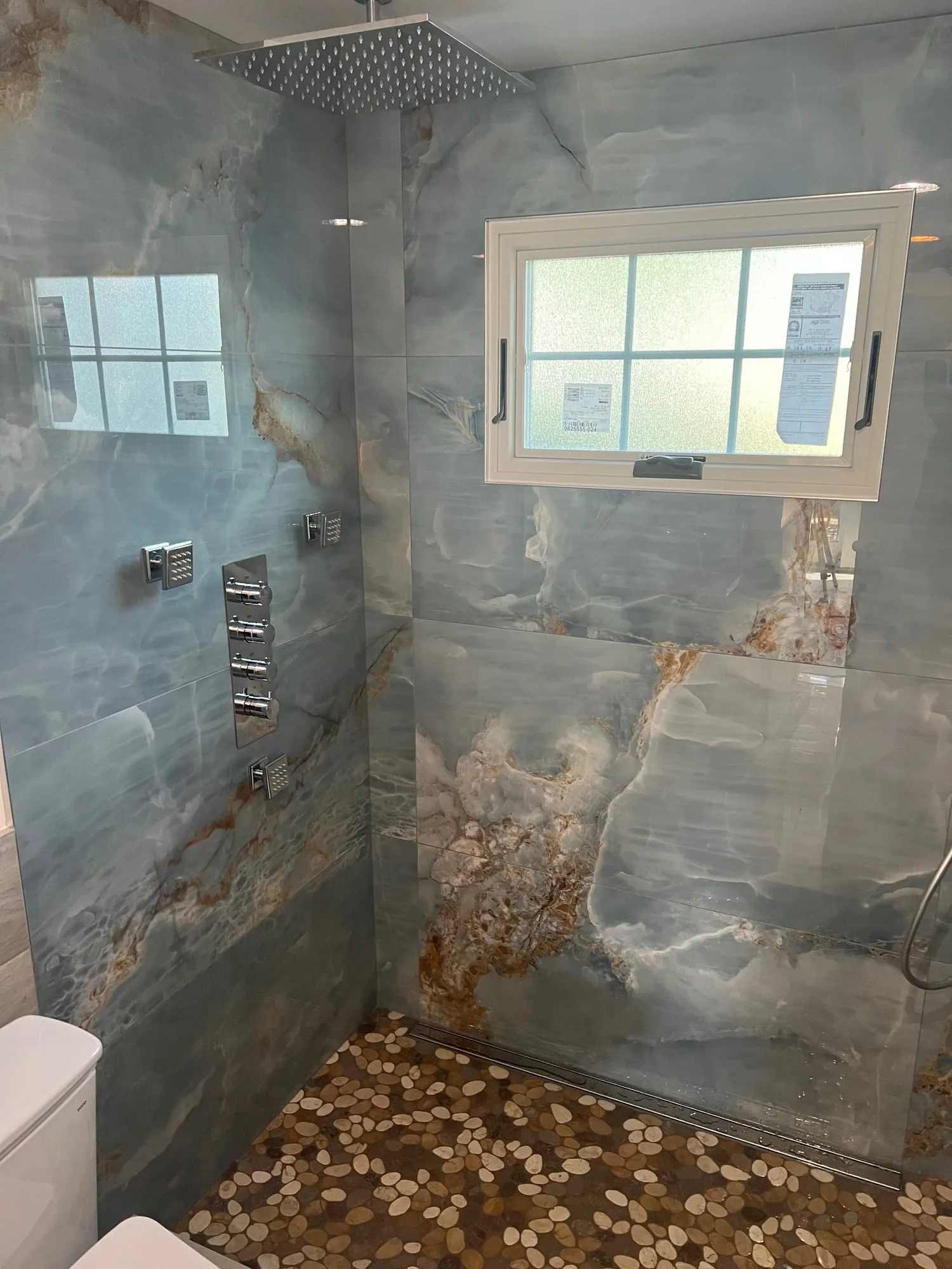 Nesconset shower with blue onyx-look porcelain walls and a pebble floor