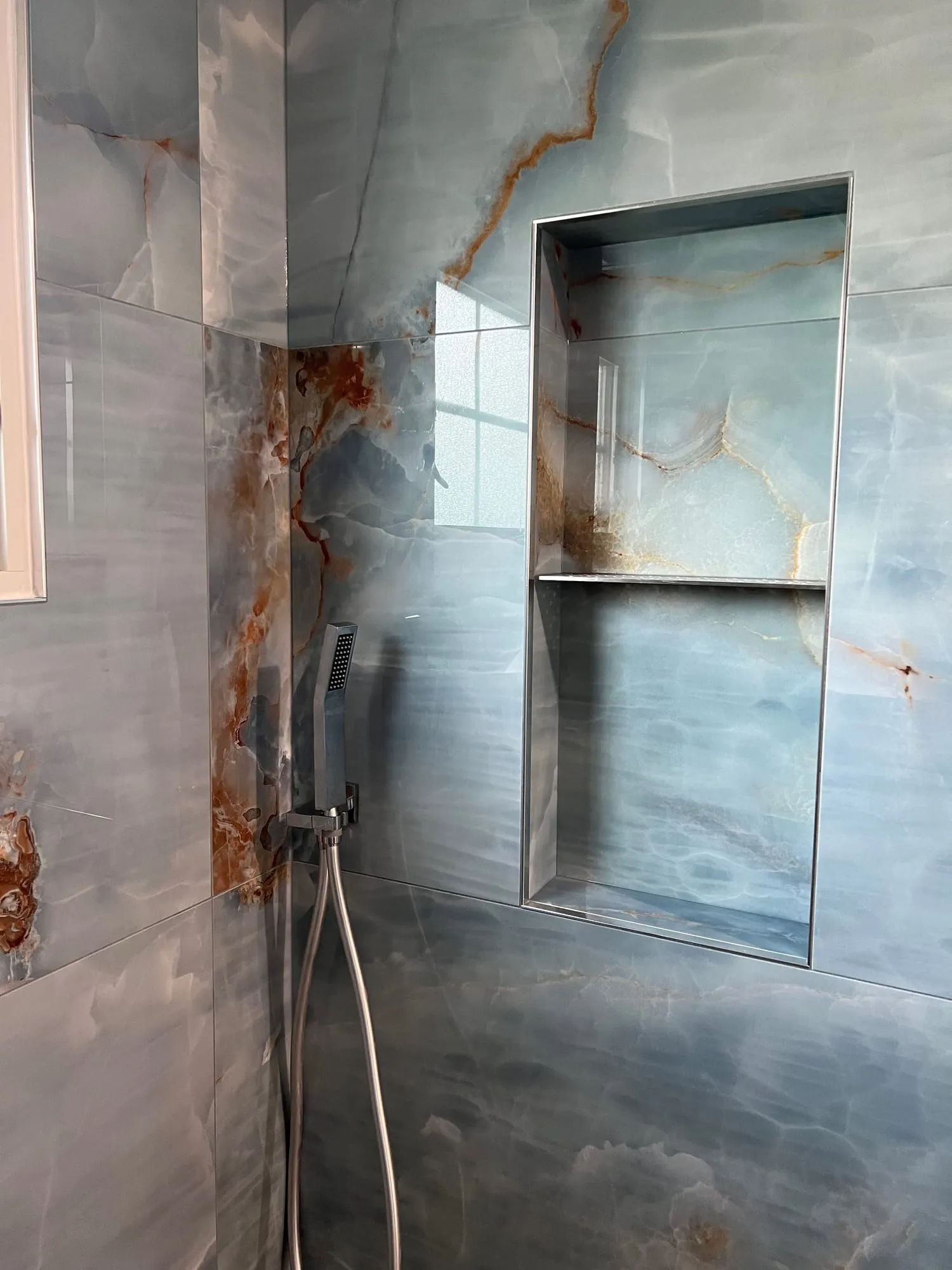 Tall recessed shower niche lined in onyx-look tile with a slim metal edge