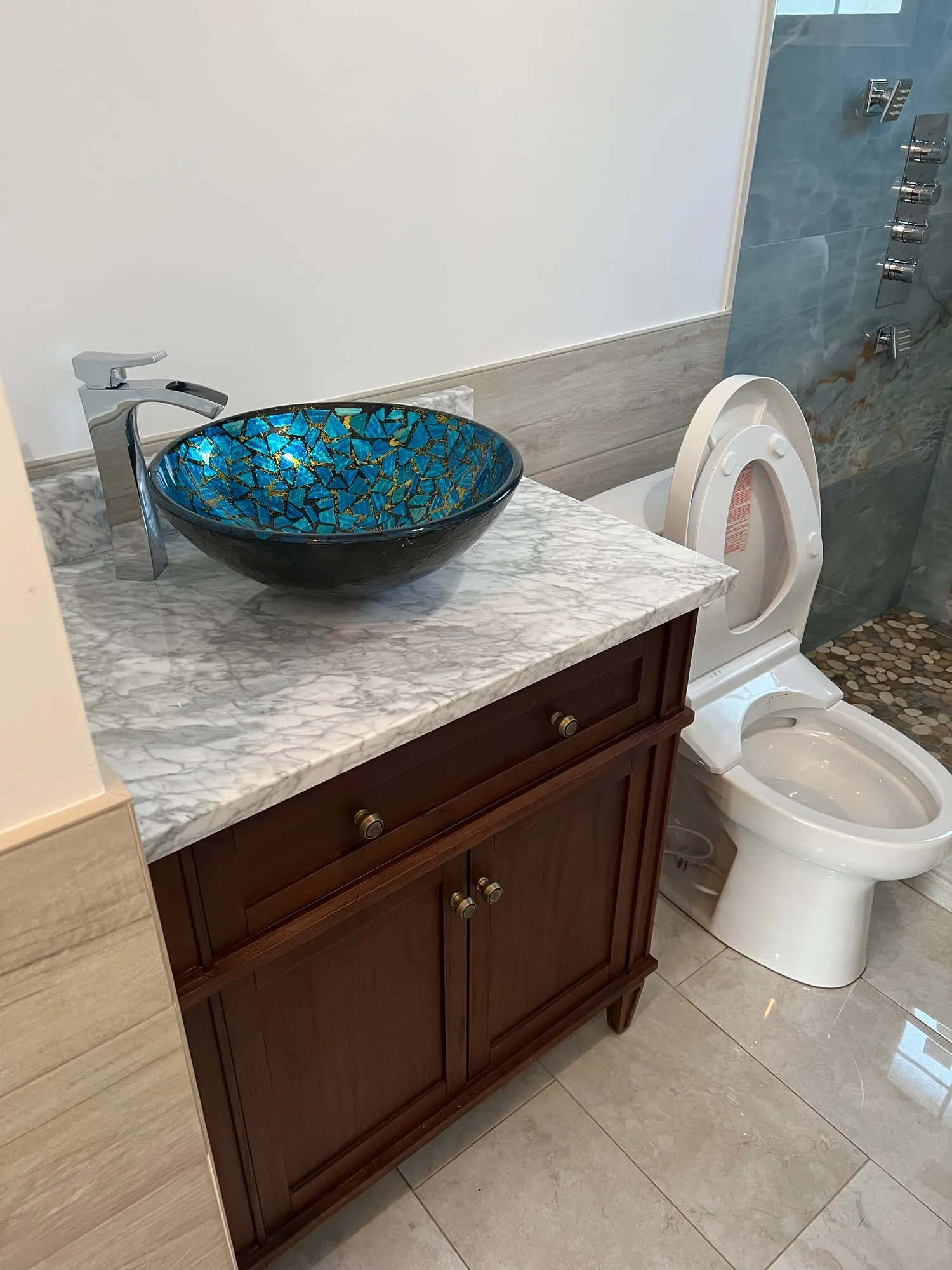 Wood vanity with a marble-look top and a blue glass vessel sink