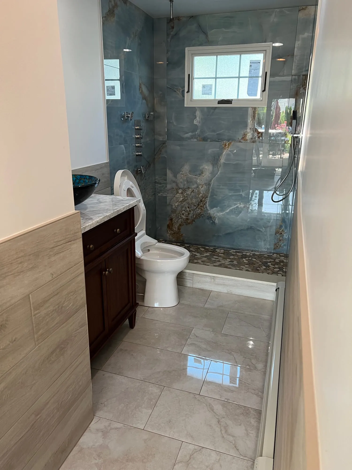 Long view of the bathroom with polished floor tile, wood-look wainscot and vanity