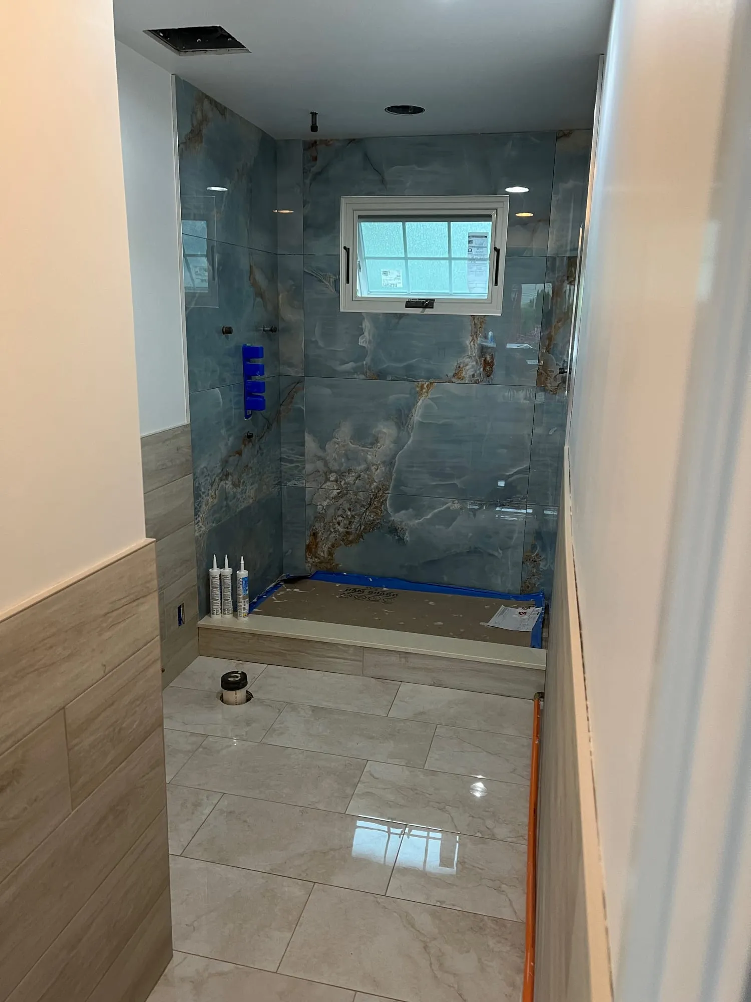 Glass-enclosed shower at the end of the bathroom, with polished large-format floor tile