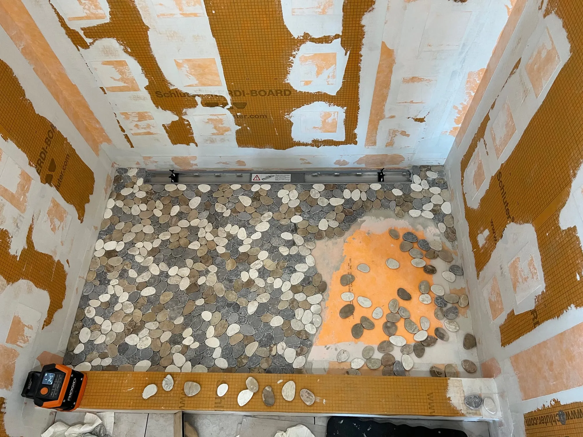 Shower walls covered in orange waterproofing membrane with a pebble floor being set