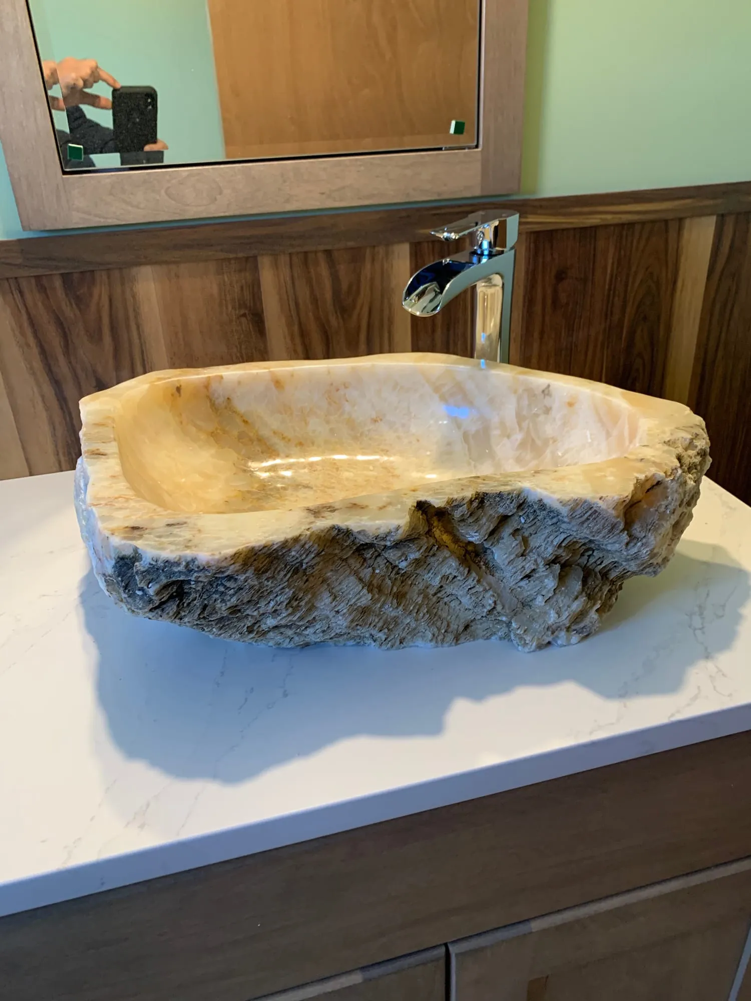 Natural stone vessel sink with a waterfall faucet on a white countertop
