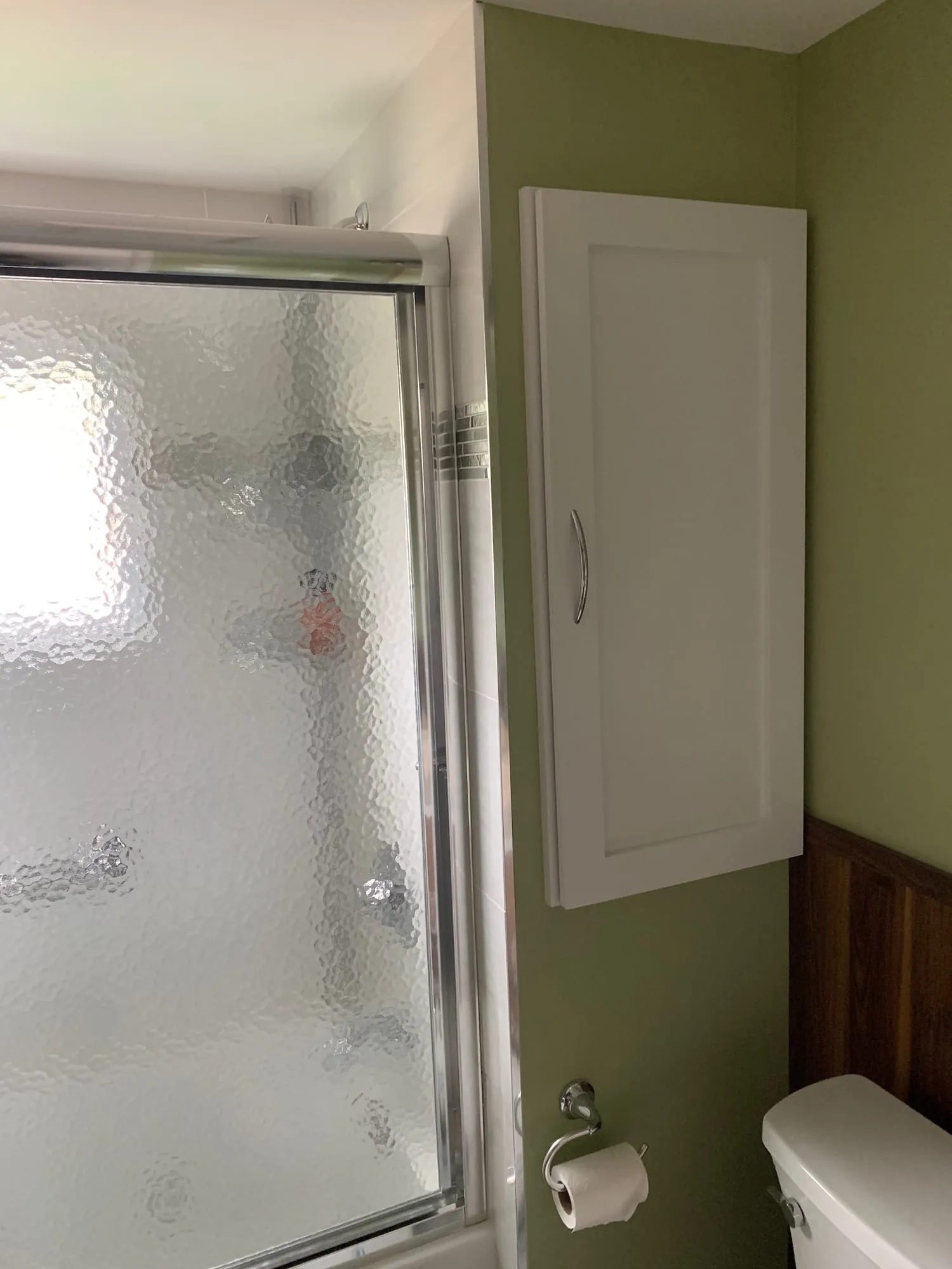 Frosted glass tub enclosure and a white wall cabinet above the toilet
